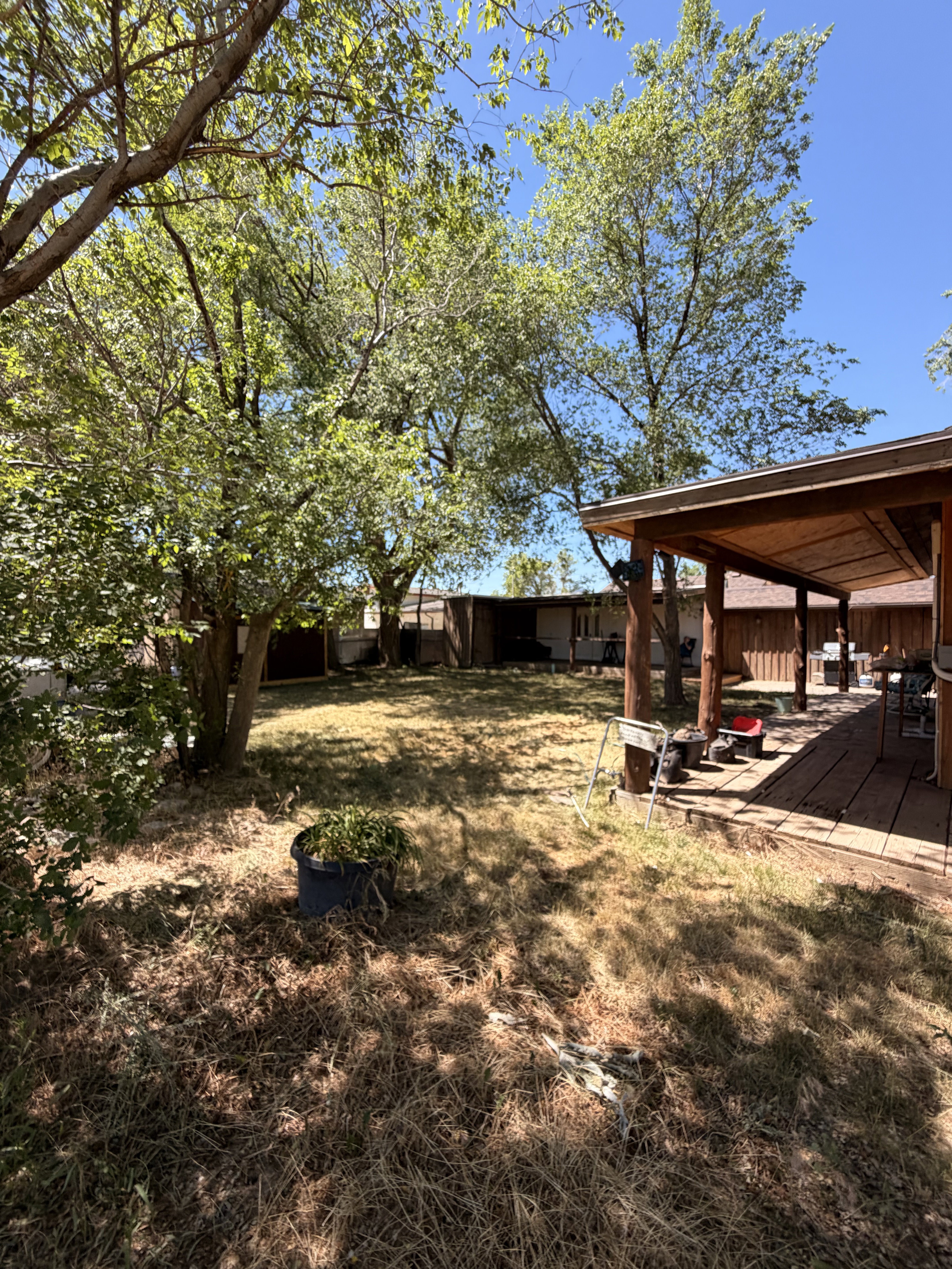 Expansive outdoor space featuring a covered wood deck, mature trees, and a wooden privacy fence