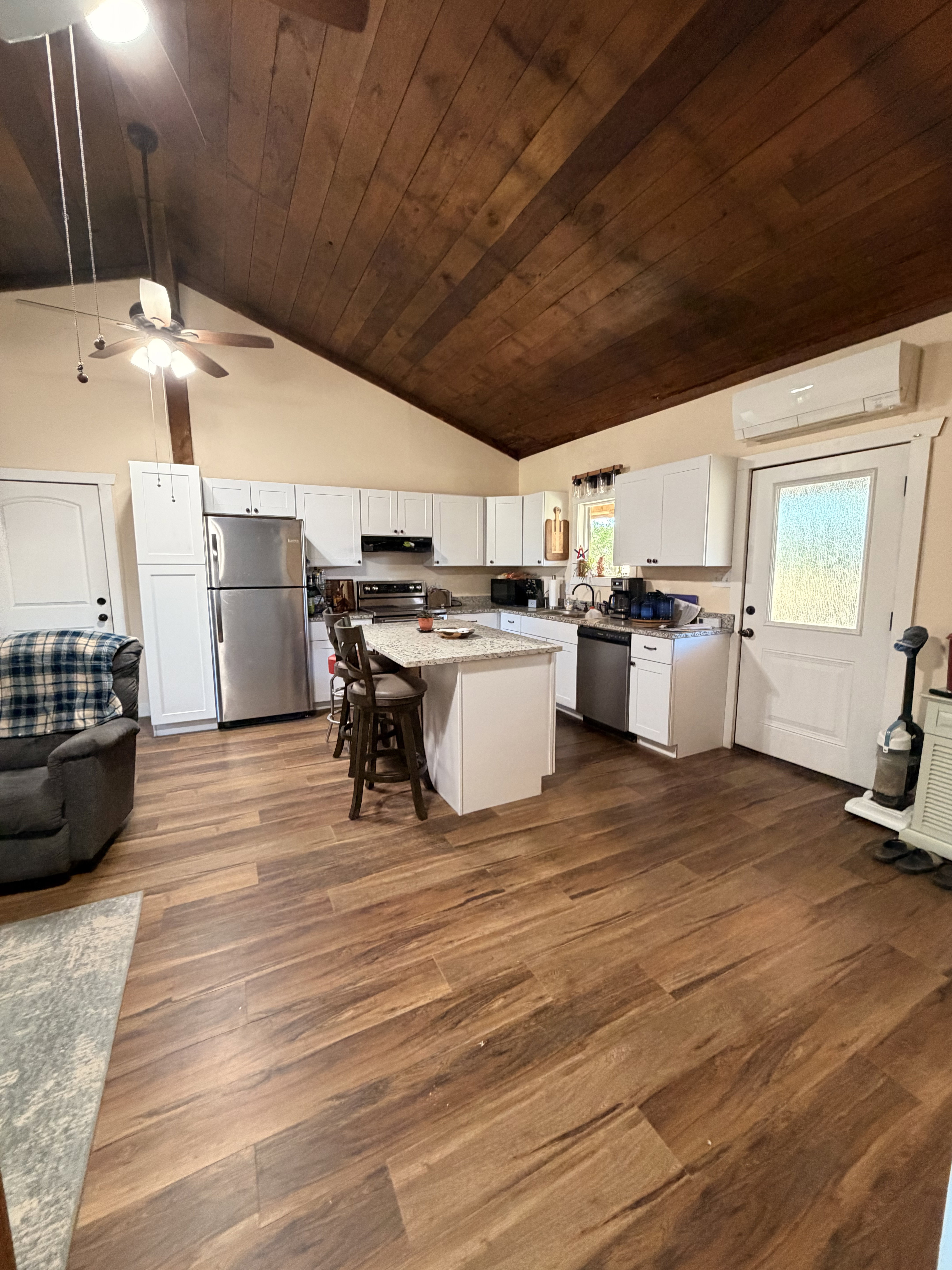 Kitchen featuring a vaulted wood-panel ceiling, wood-finish flooring, white cabinetry, a central island with a granite-style countertop, and stainless steel appliances