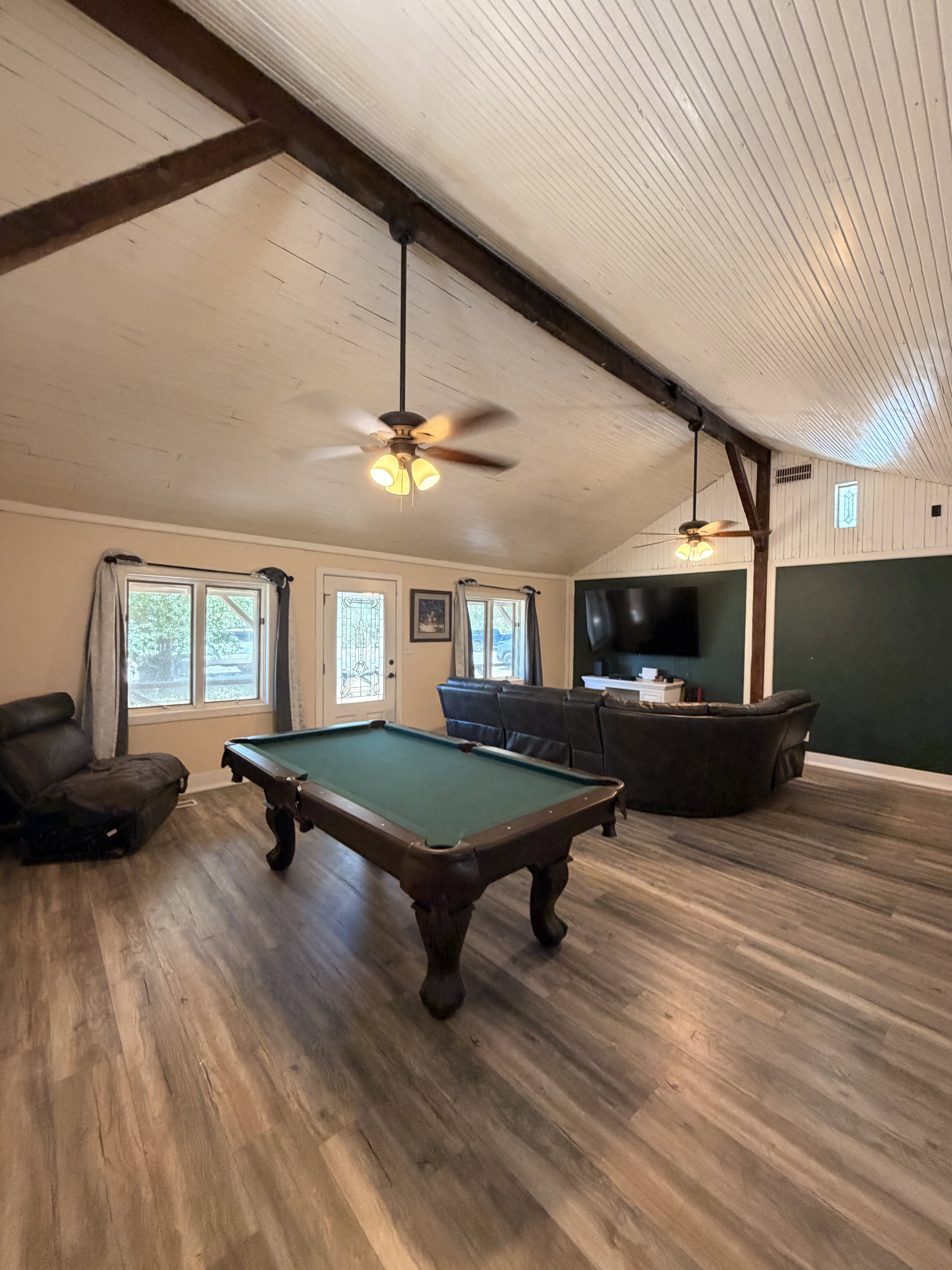 Spacious room featuring wood-finish flooring and a white planked vaulted ceiling with exposed wood beams