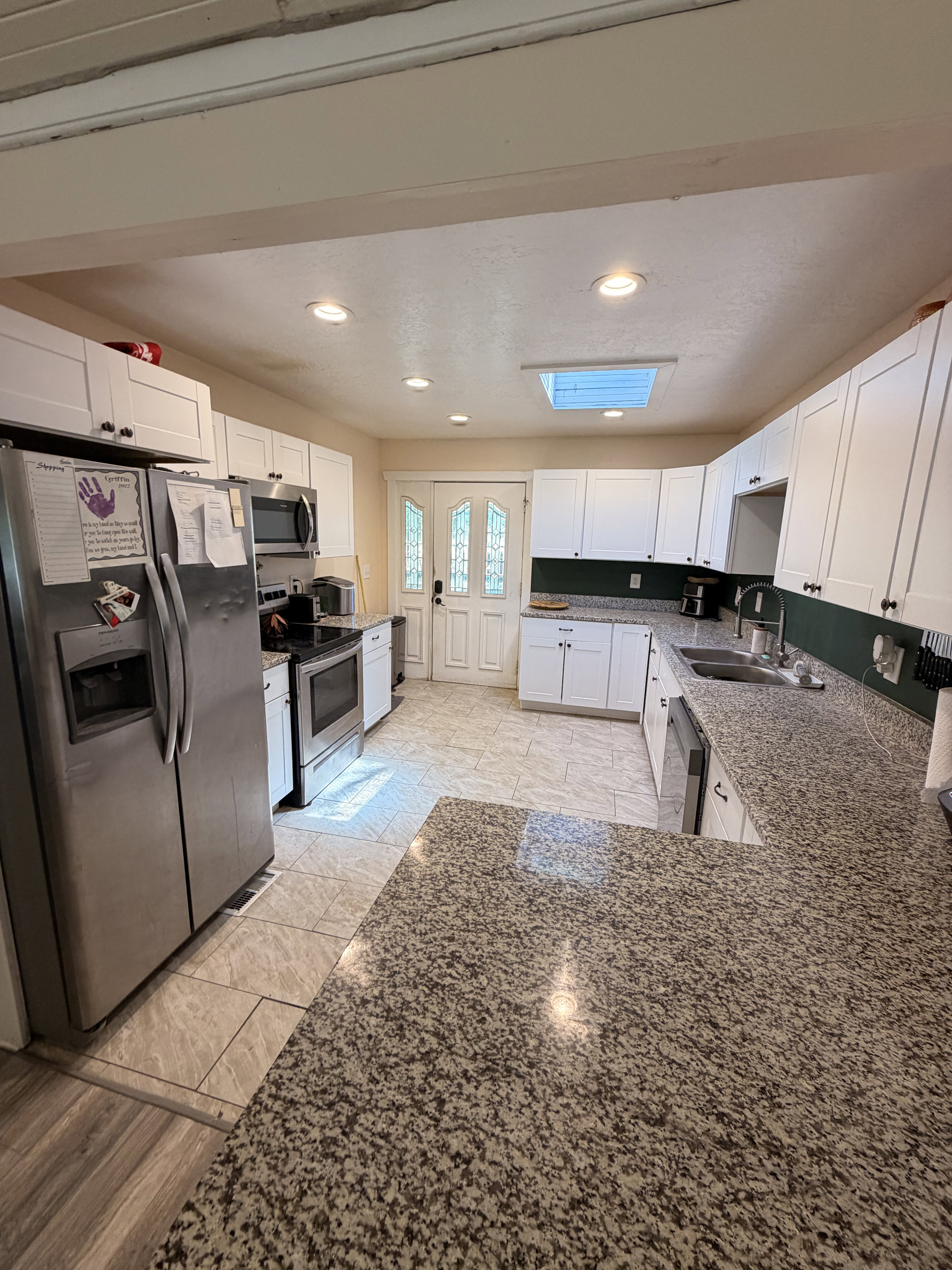 Kitchen featuring an expansive U-shaped countertop with a flecked surface, white shaker-style cabinetry, and stainless steel appliances