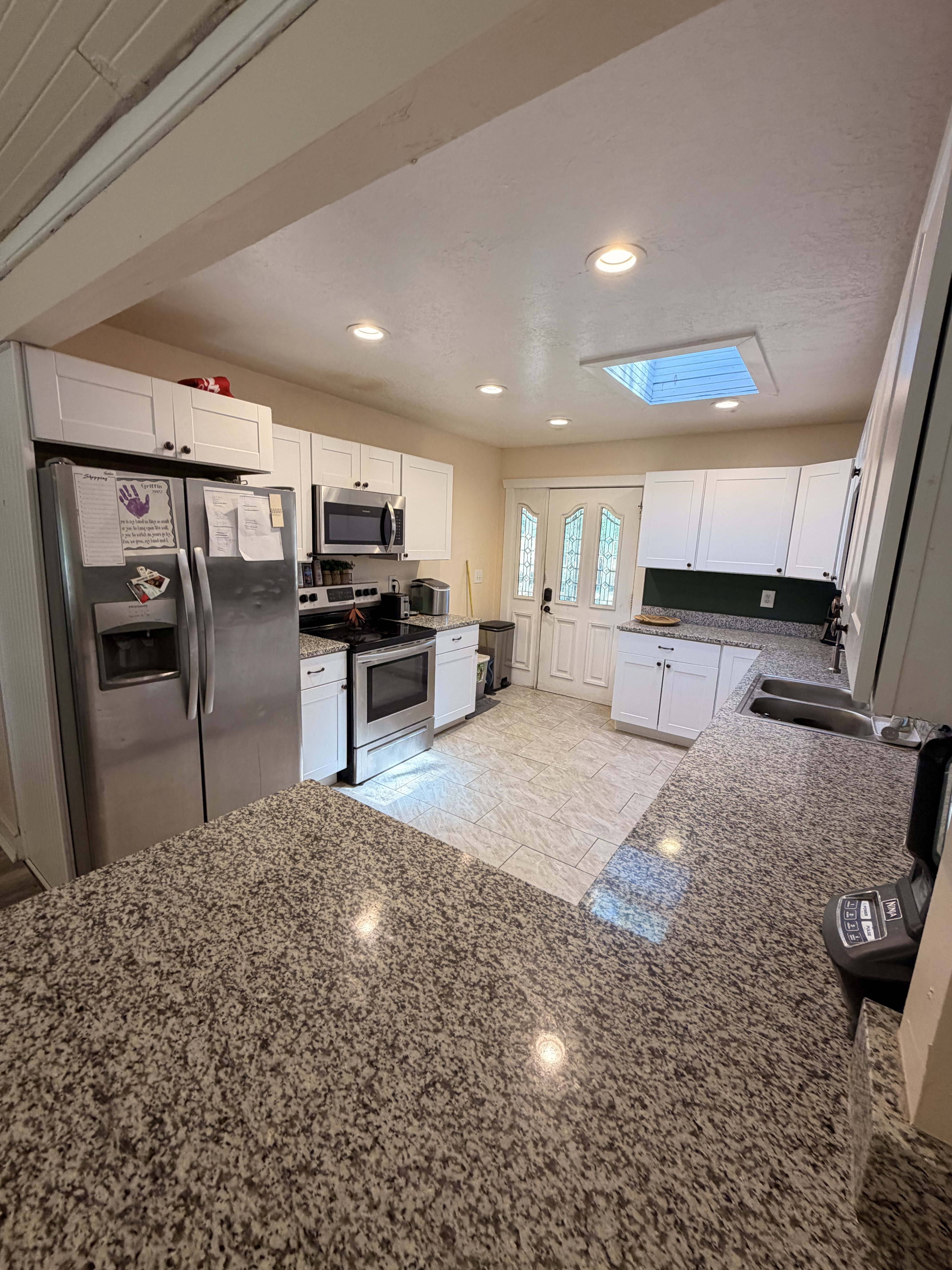 Kitchen featuring extensive counter space with a speckled stone finish, white cabinetry, stainless steel appliances, and a skylight