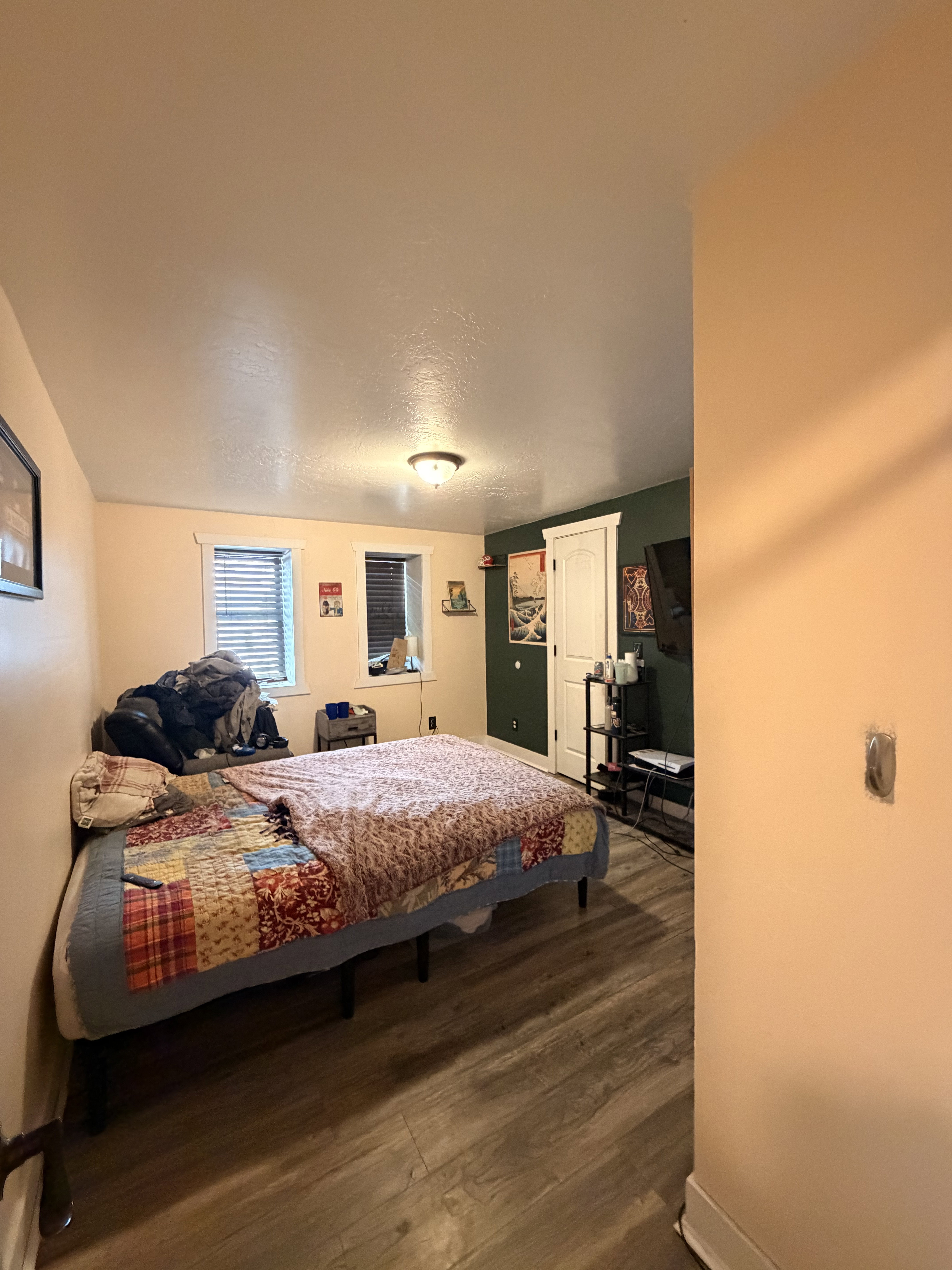 Bedroom with wood-finish flooring, two windows with blinds, a prominent accent wall, and a white paneled door