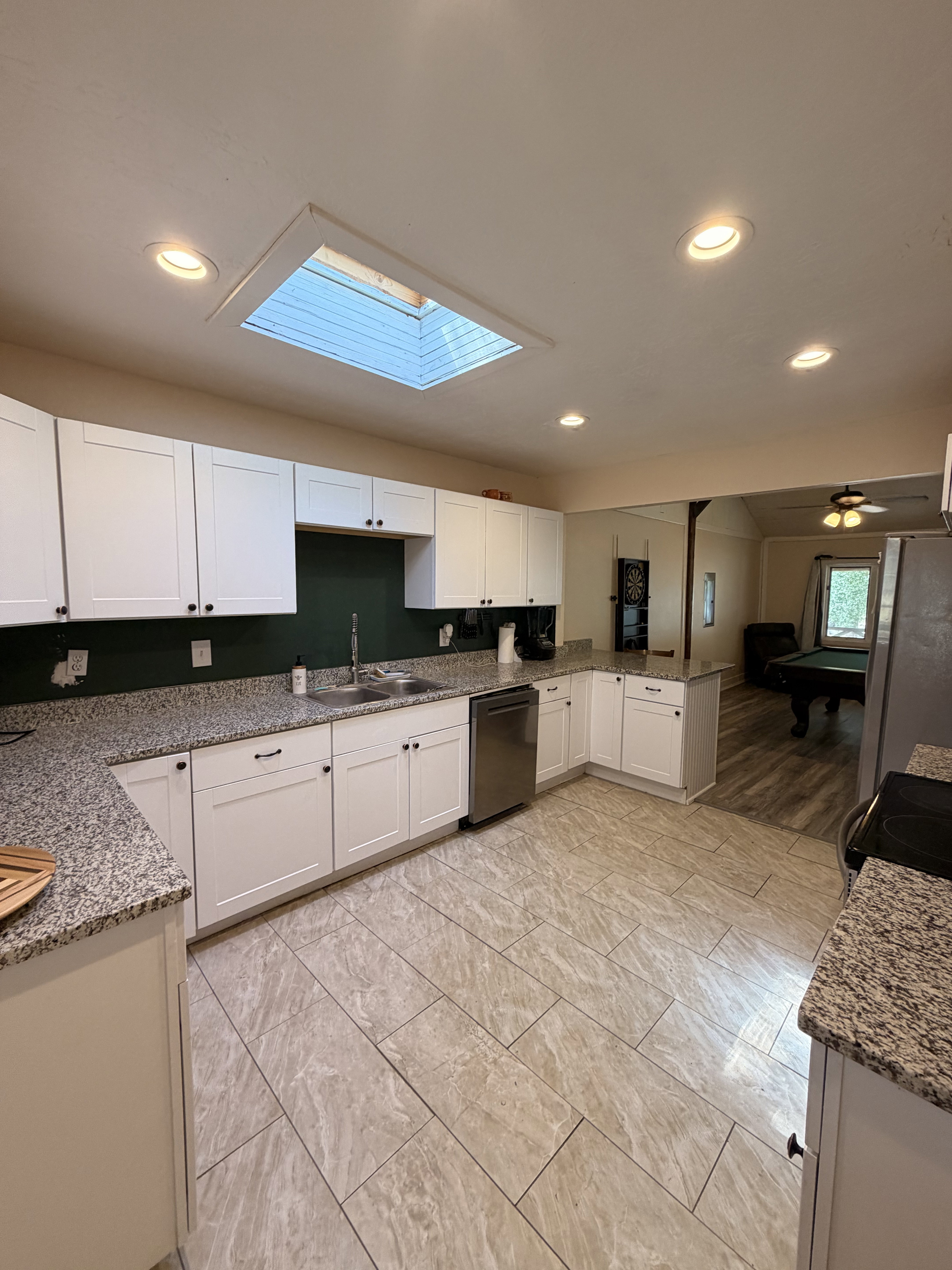 Modern kitchen featuring white shaker cabinetry, speckled countertops, stainless steel dishwasher, recessed lighting, and a skylight
