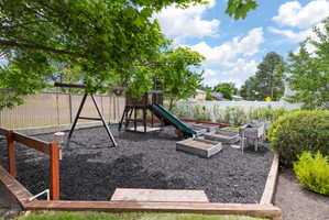 Landscaped backyard featuring a swing set, playset with slide, and multiple raised garden beds