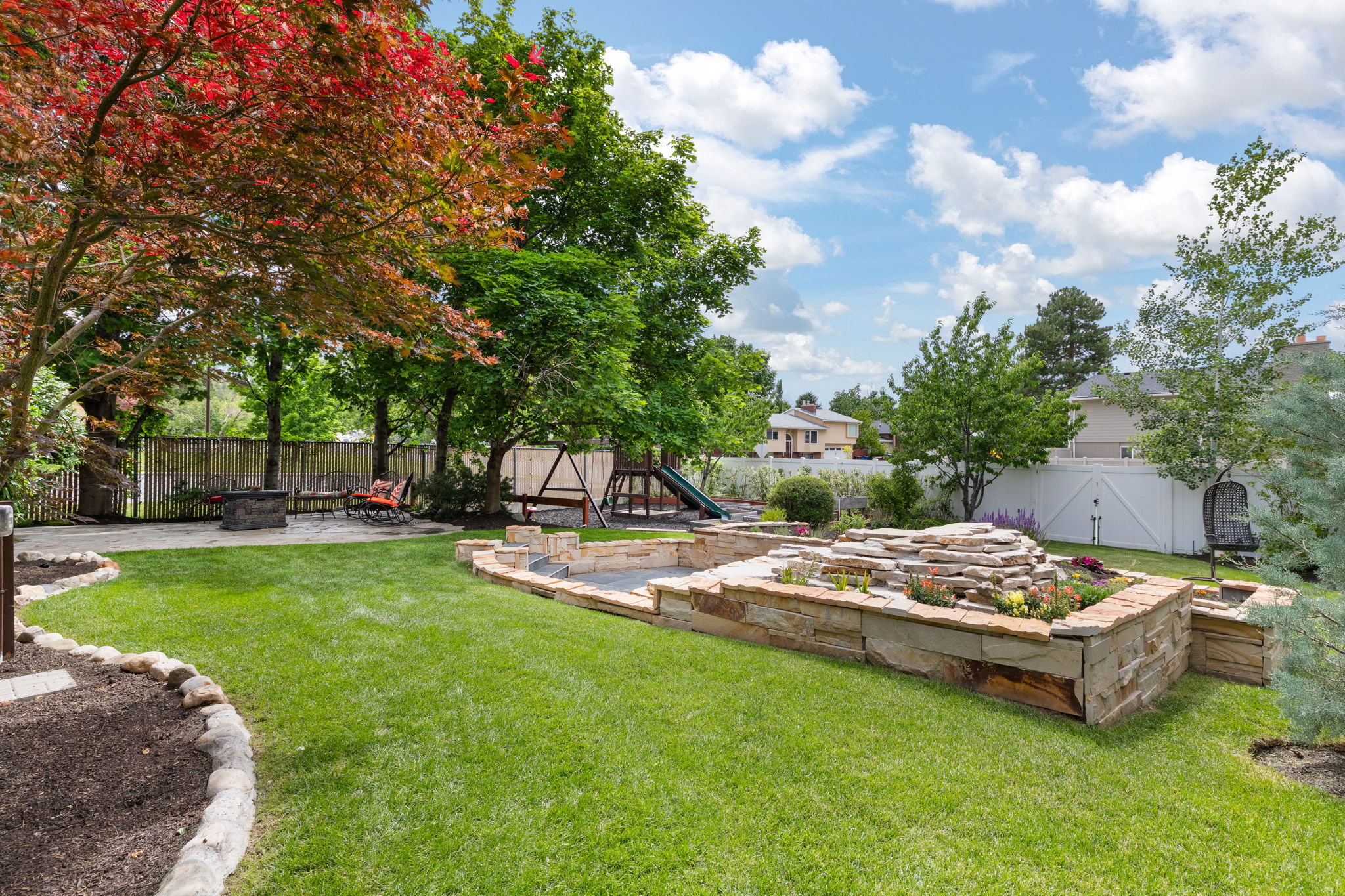 Expansive backyard featuring a lush lawn, mature trees, and a multi-tiered stone planter
