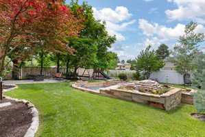 Expansive backyard featuring a lush lawn, mature trees, and a multi-tiered stone planter