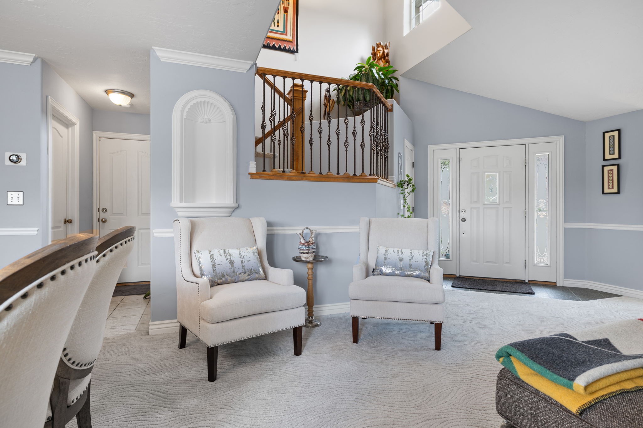 Two-story foyer with a decorative arched wall niche, hardwood and wrought iron staircase, and a front entry door with decorative glass sidelights