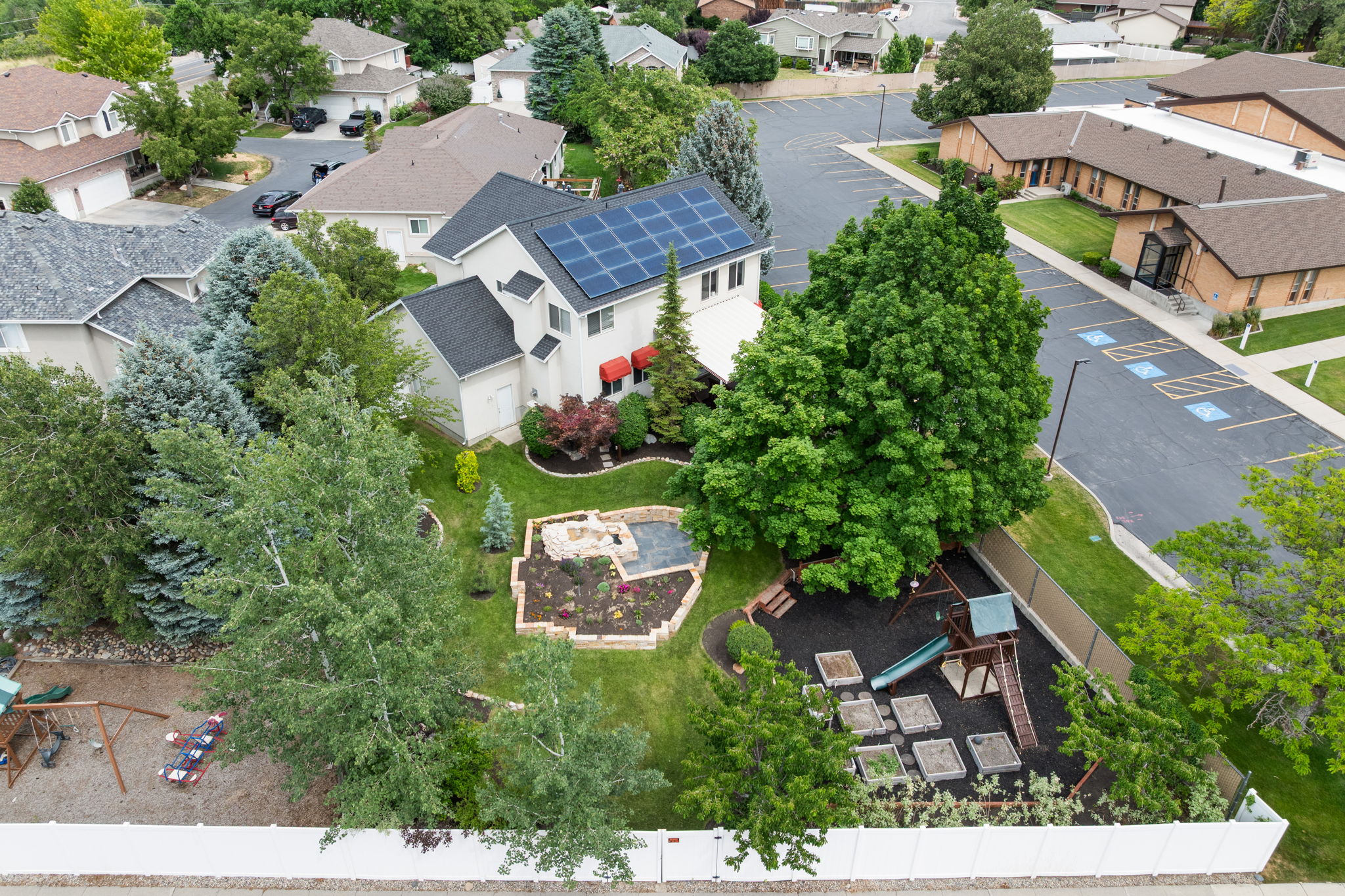 Two-story residence with solar panels on the roof, featuring a landscaped backyard with a raised garden bed, a fire pit area, and mature trees