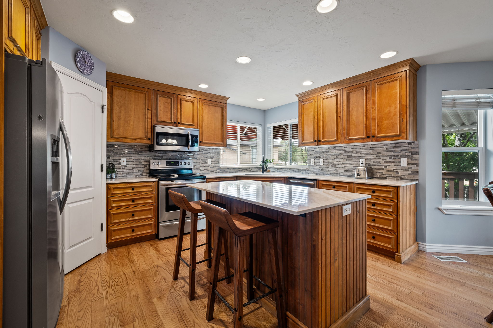 Kitchen featuring brown cabinets, stainless steel appliances, decorative backsplash, light stone counters, and recessed lighting