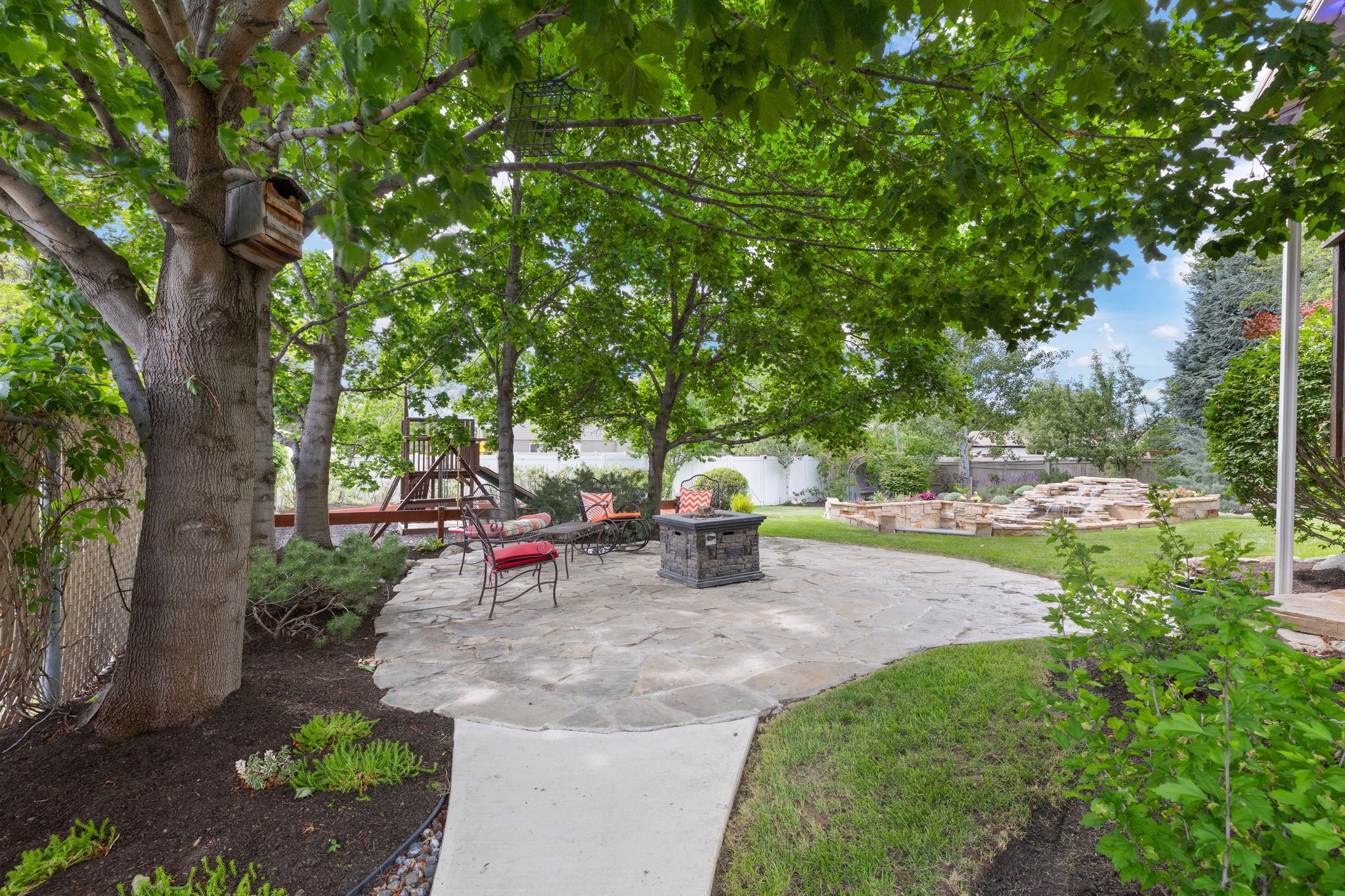 Expansive backyard featuring a natural stone patio, mature trees, and a manicured lawn