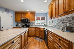 Kitchen with brown cabinets, light stone counters, light wood-style flooring, recessed lighting, and decorative backsplash