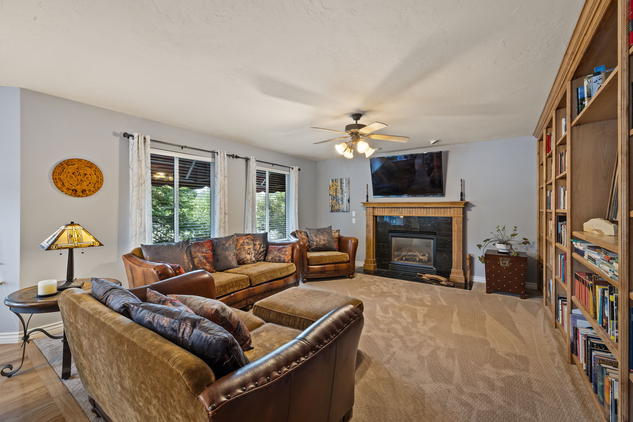 Living area featuring a tiled fireplace, a ceiling fan, and light carpet