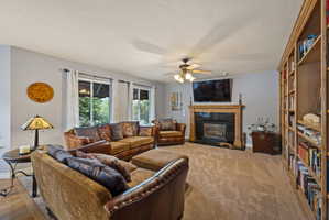 Living area featuring a tiled fireplace, a ceiling fan, and light carpet