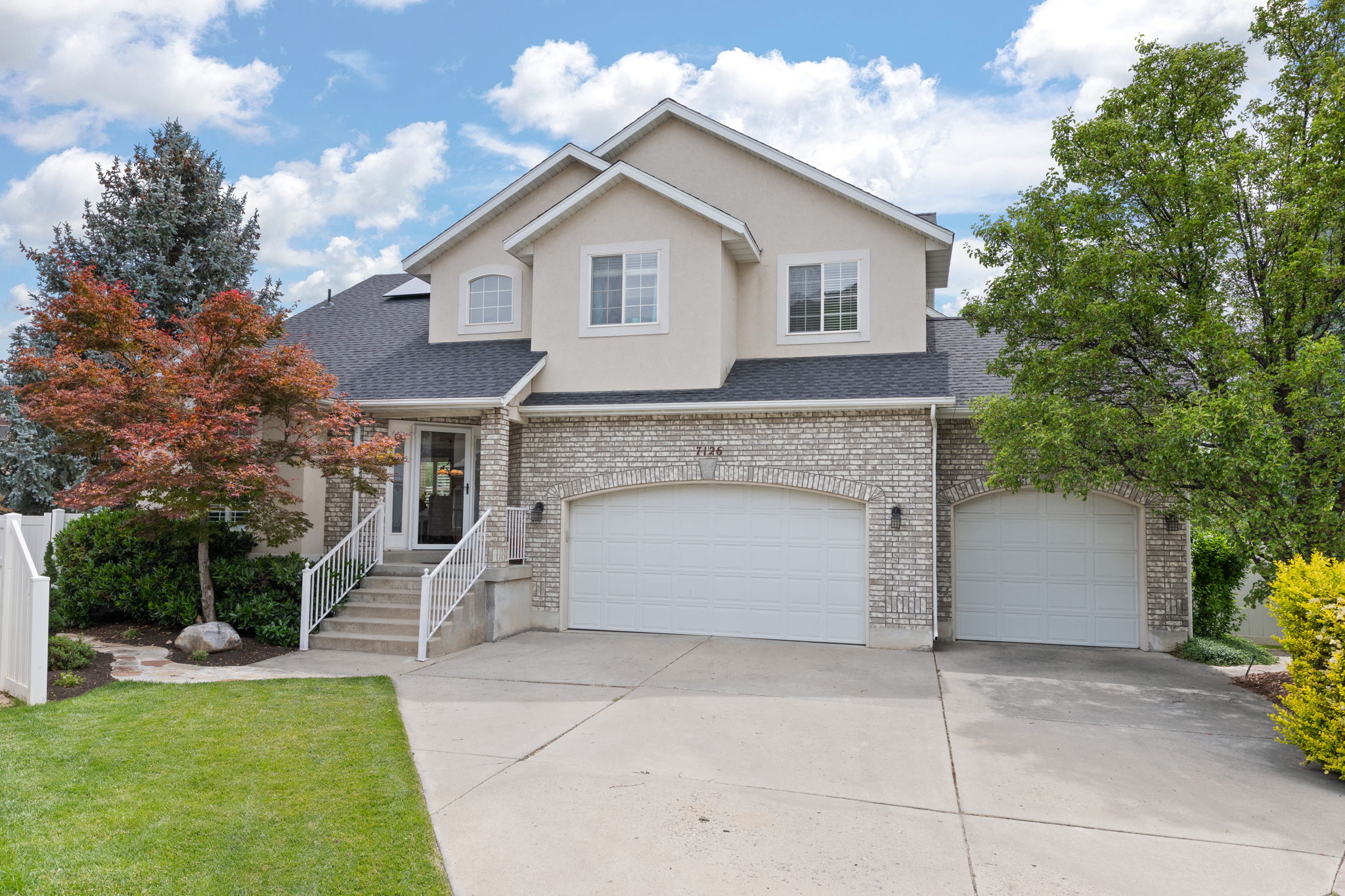 Traditional-style house with brick siding, concrete driveway, an attached garage, solar panels, and stucco siding