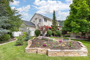 Expansive backyard featuring tiered landscaping with stone retaining walls, mature trees, and a manicured lawn,