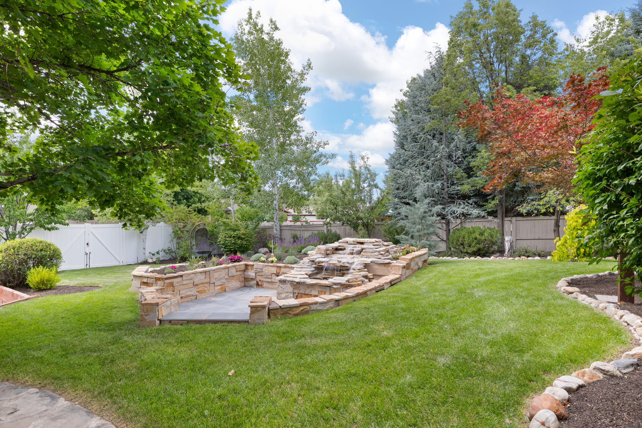 Expansive green lawn with a tiered stone patio and a decorative rock water feature