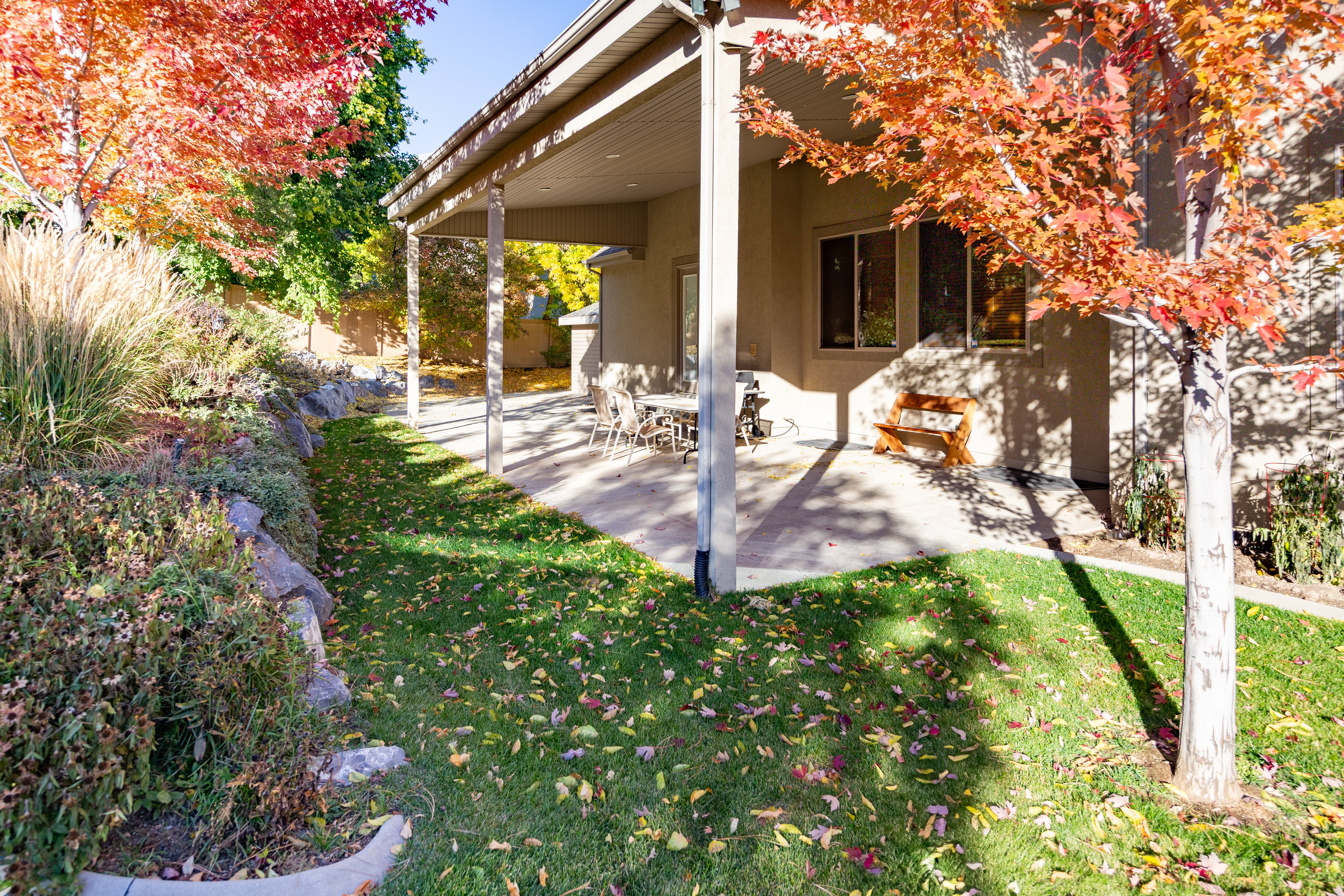 Expansive rear patio featuring a covered area with support pillars, mature landscaping, and a lawn
