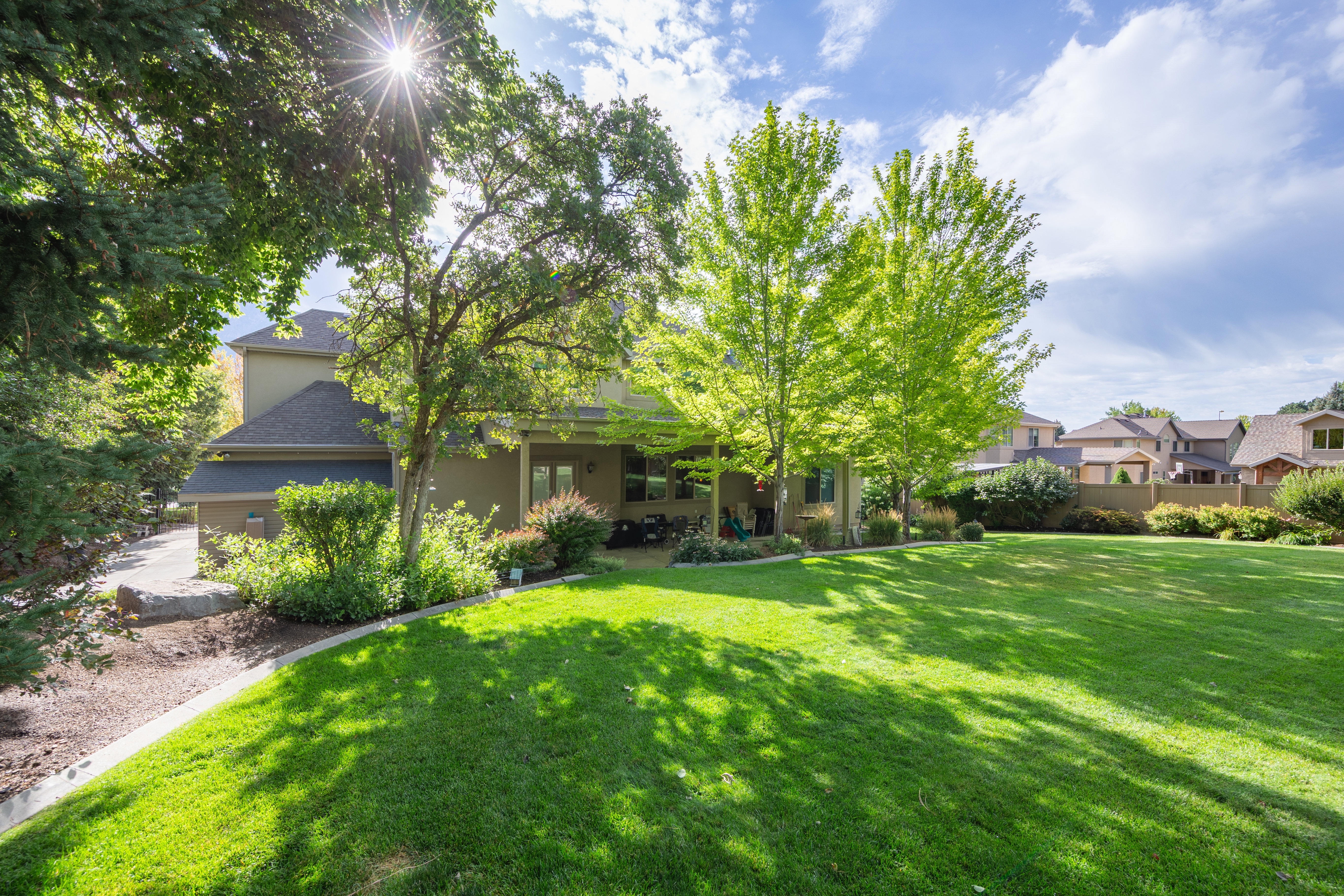 Expansive lawn with mature trees, offering a covered patio area and a visible side entrance