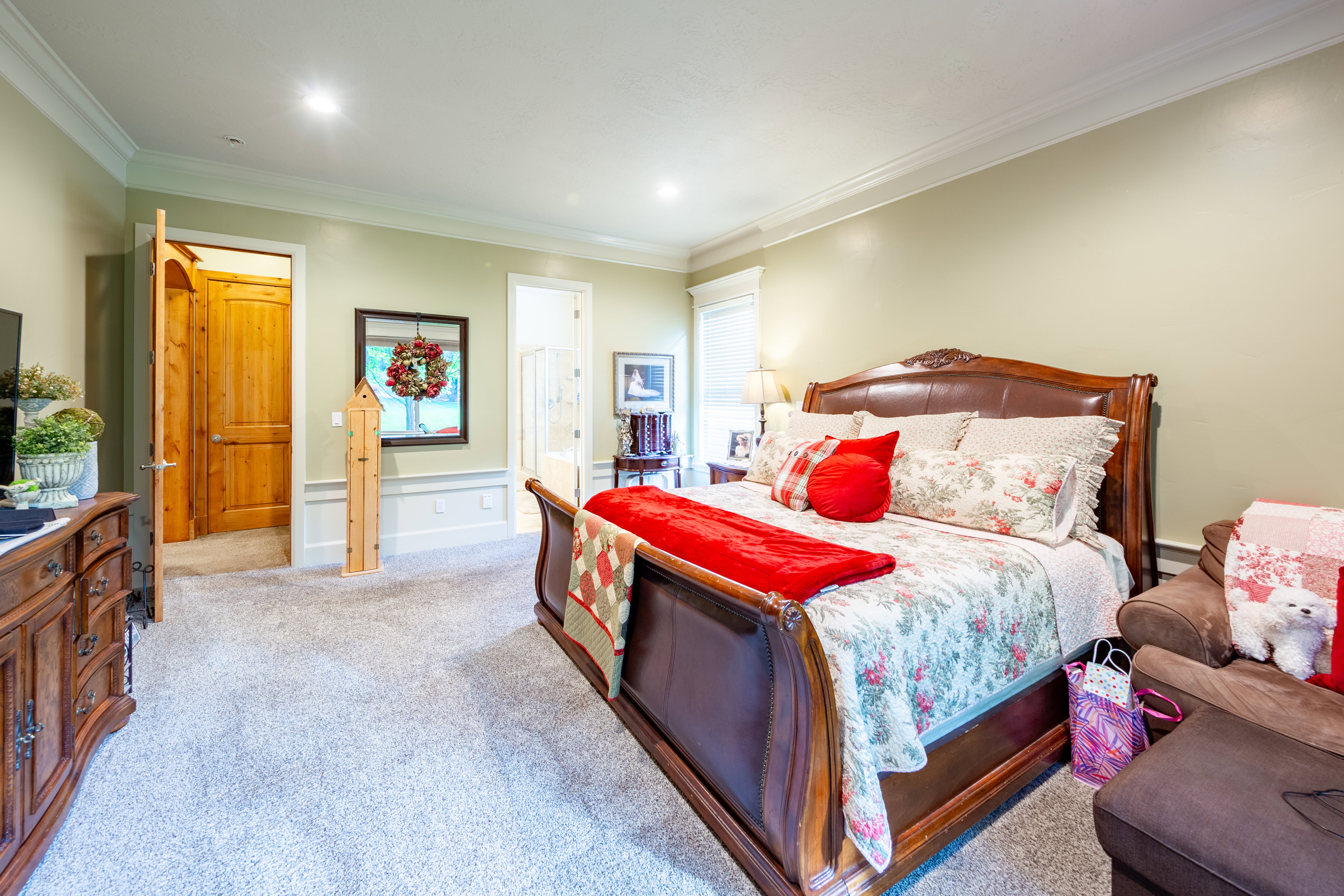 Spacious bedroom featuring light neutral wall paint, crown molding, recessed lighting, carpet flooring, and a wood-finish door with an arched top