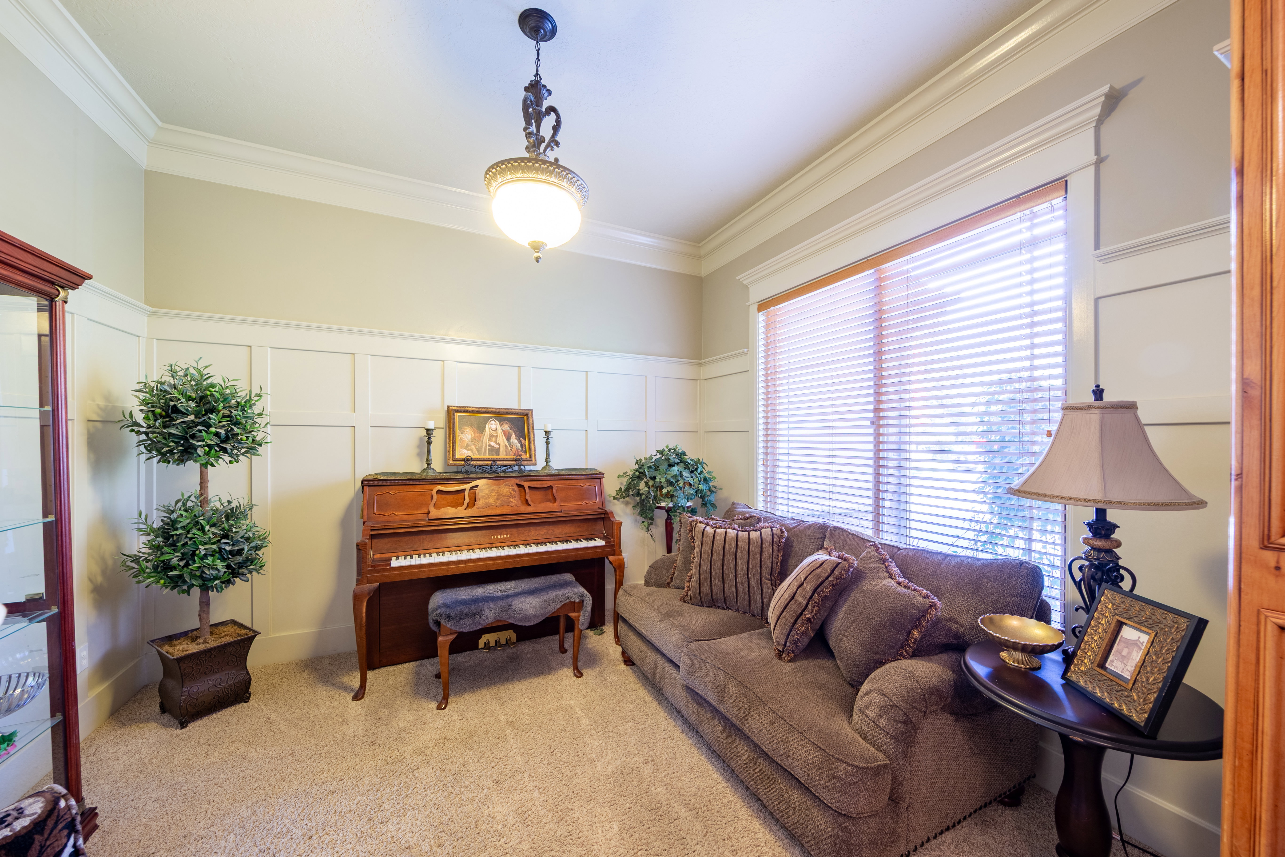 Carpeted interior space featuring wainscoting, crown molding, a large window with blinds, and an ornate ceiling light fixture