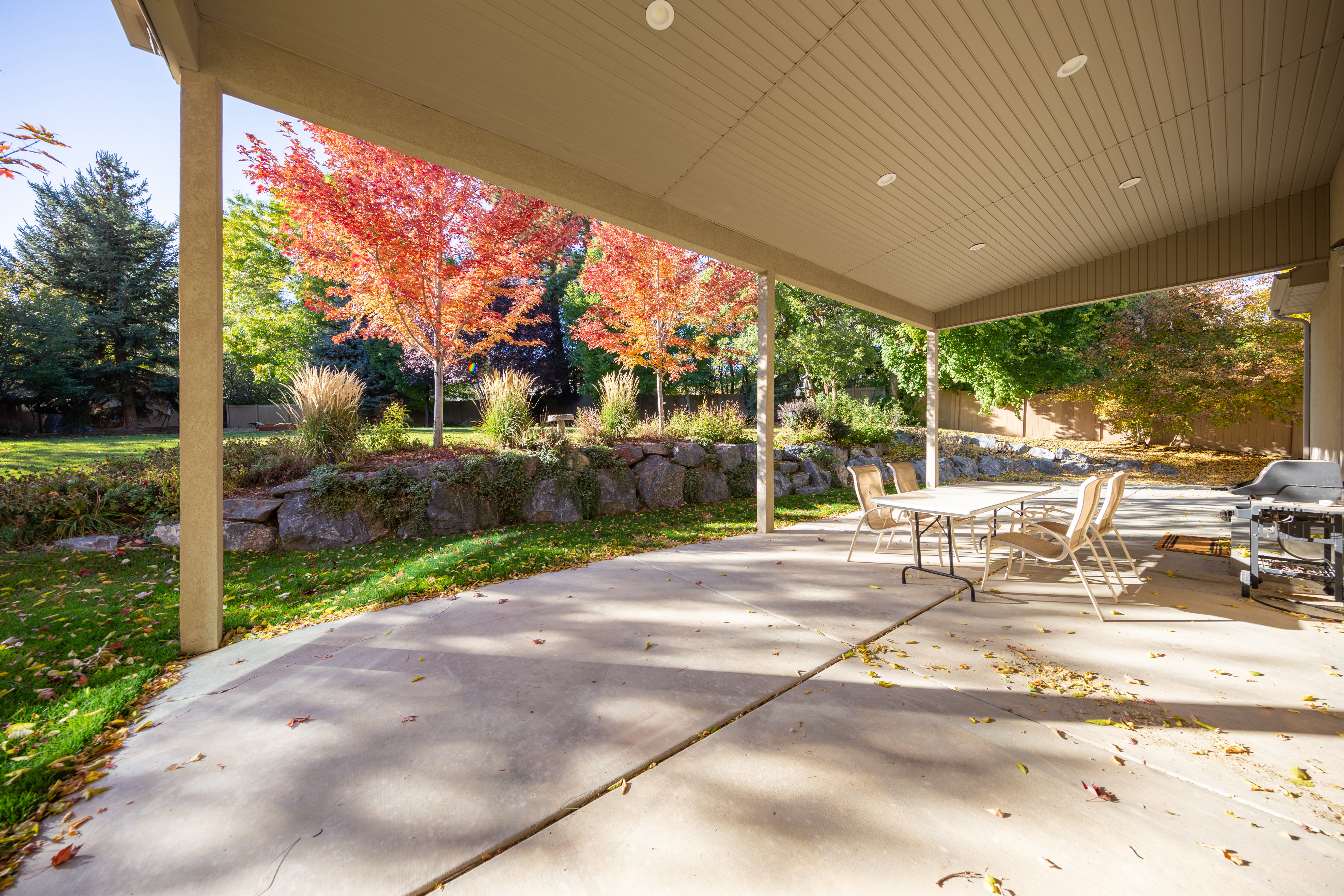 Covered patio featuring recessed lighting, a concrete surface, and direct access to a landscaped backyard with a rock retaining wall and mature trees