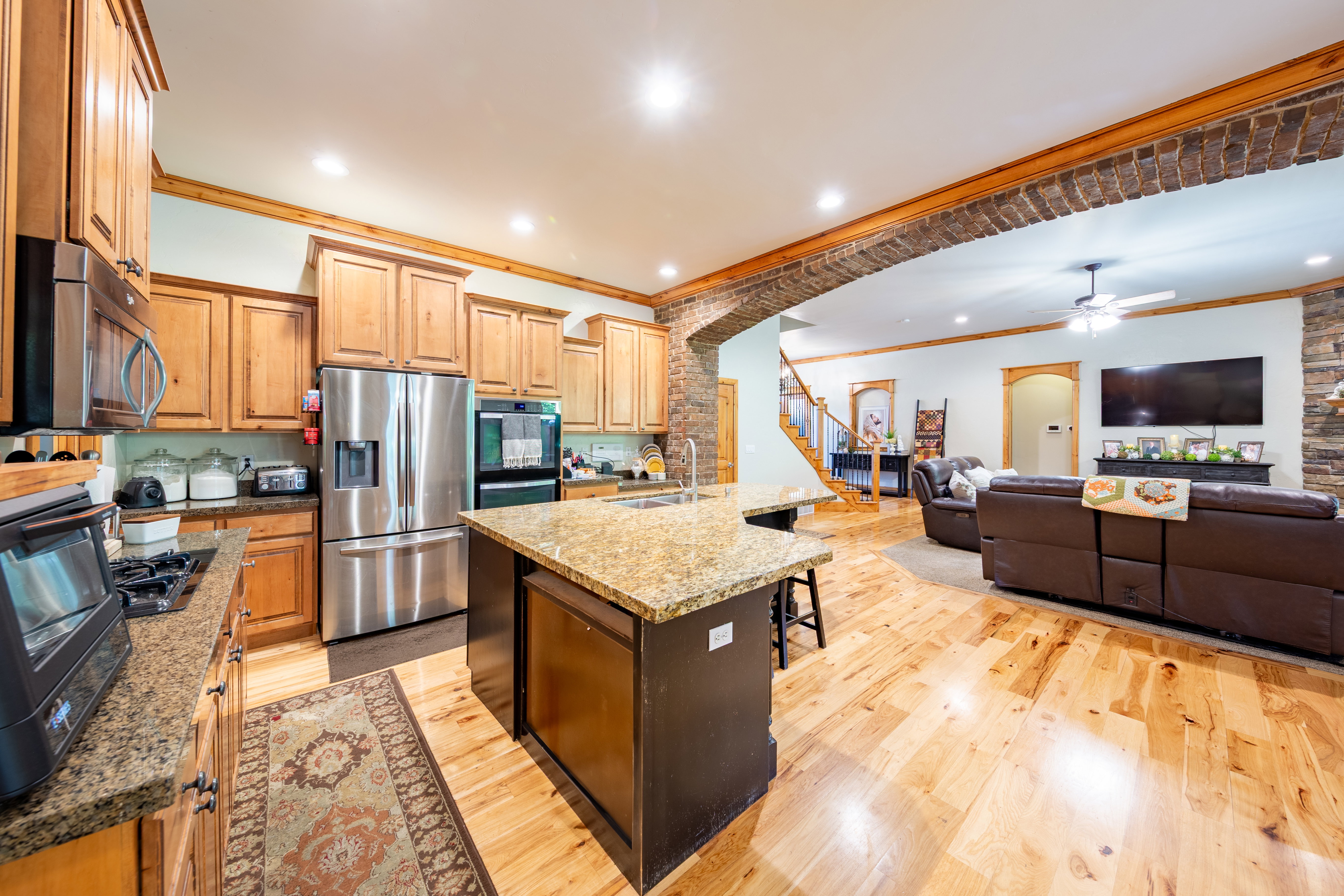 Open-concept kitchen featuring wood-finish cabinetry, granite countertops, stainless steel appliances, and a central island with seating