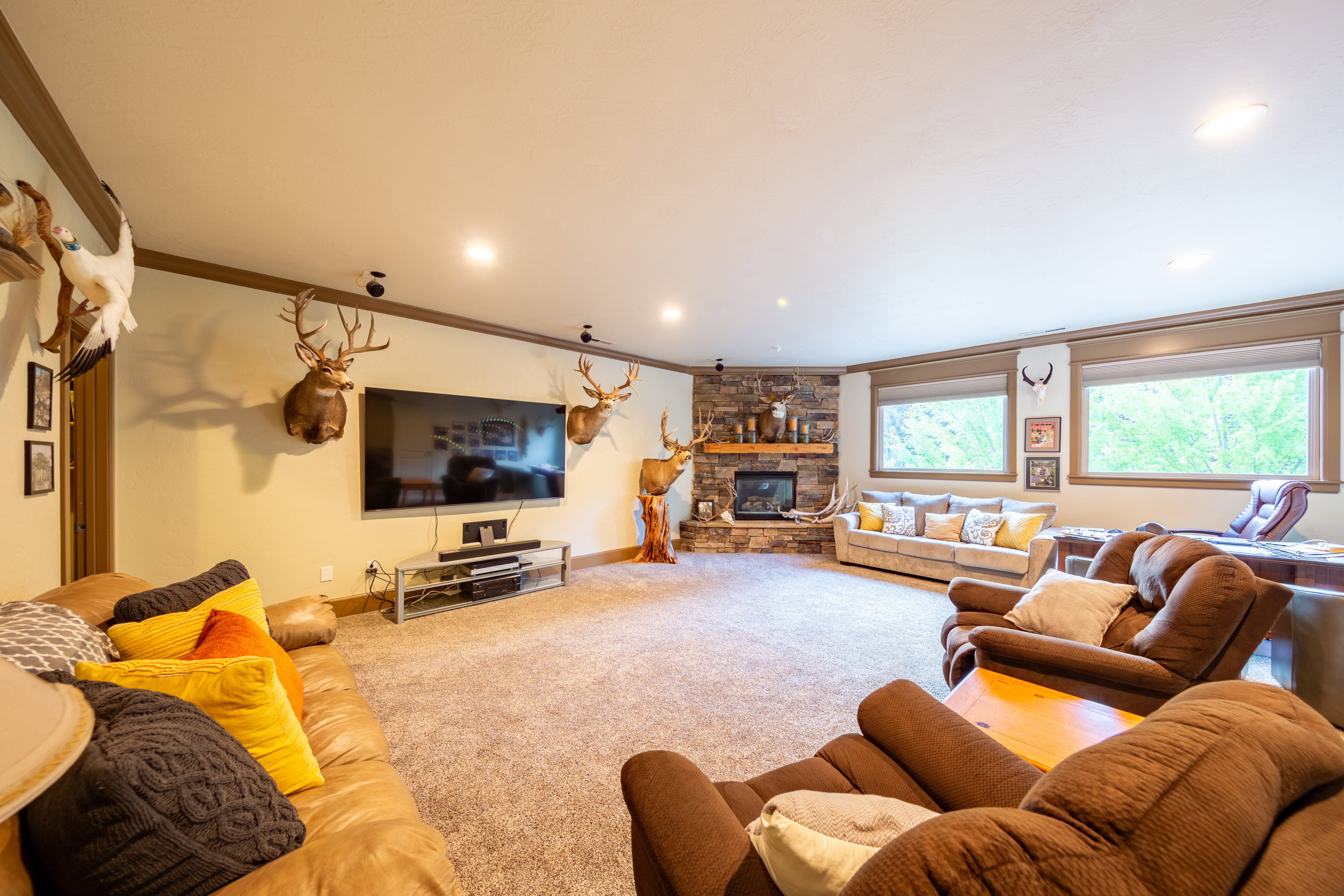 Spacious entertainment room featuring recessed lighting, deep pile carpet flooring, and a stone-clad corner fireplace with a wood mantle