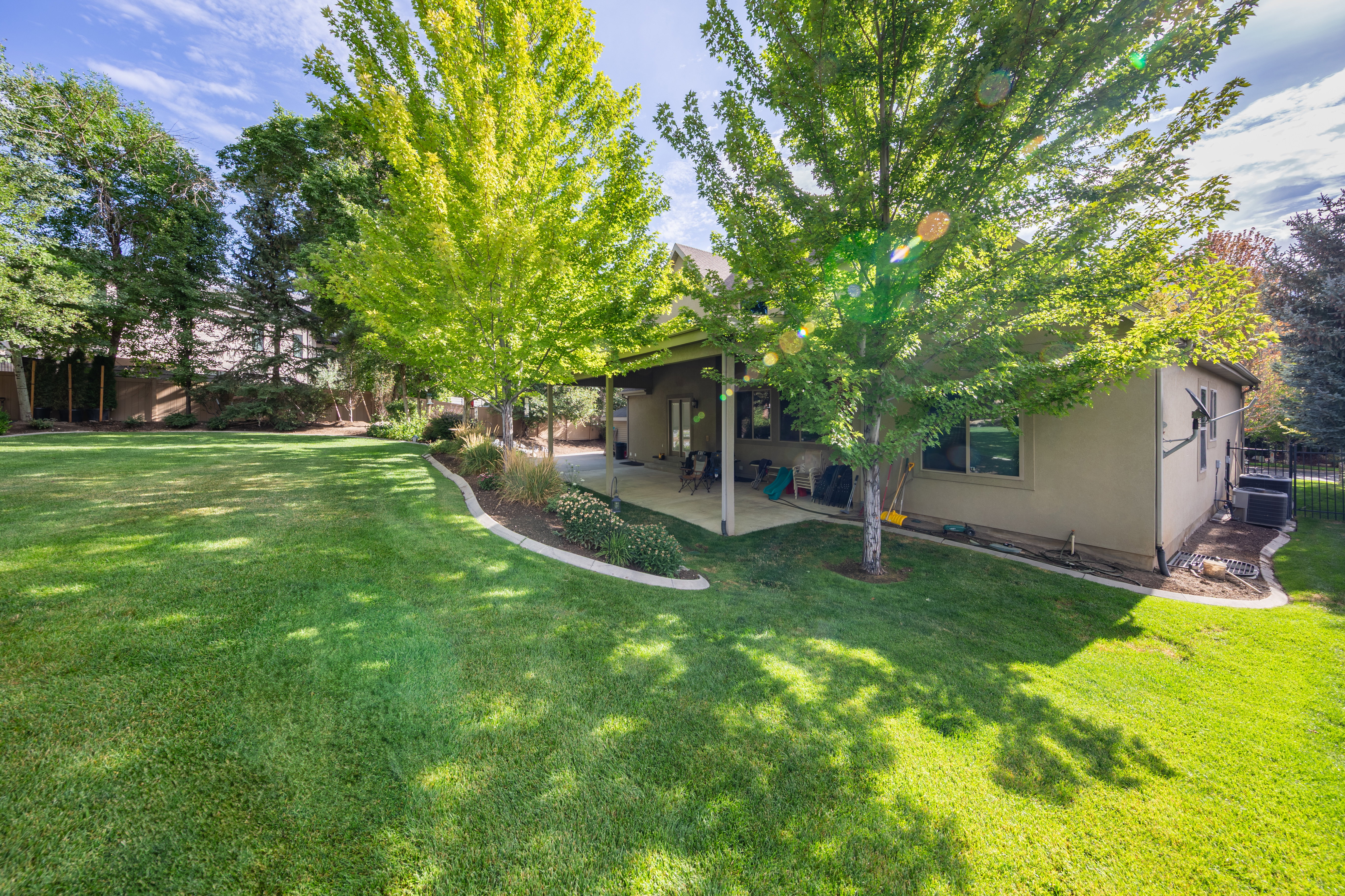 Expansive green lawn with mature shade trees and a covered patio
