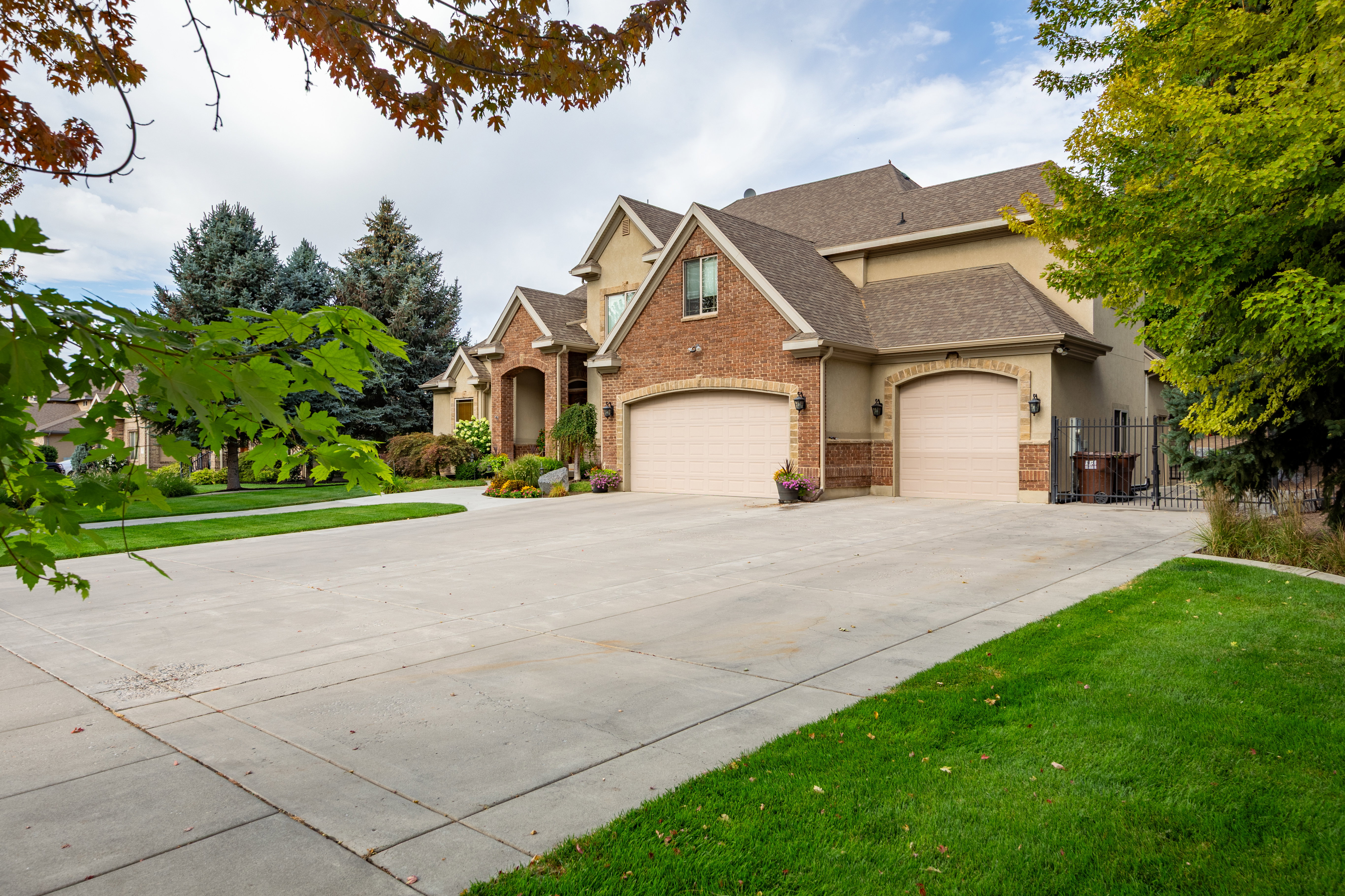 Spacious concrete driveway leading to a residence featuring a brick and stucco exterior, arched entryways, and two distinct garage doors