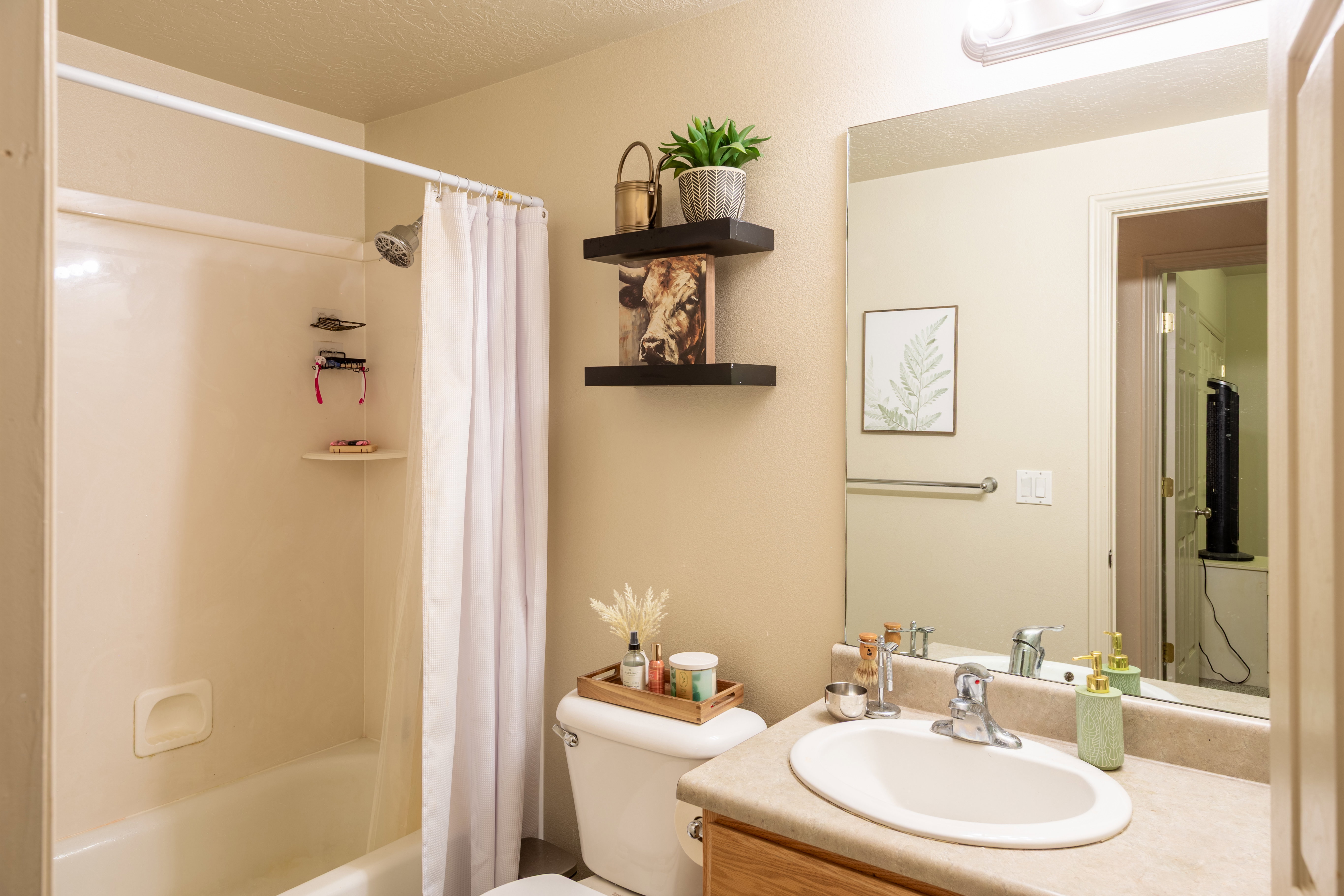 Bathroom featuring a shower-over-tub combination with a white surround, a vanity with an integrated sink, a large wall-mounted mirror, and floating shelving