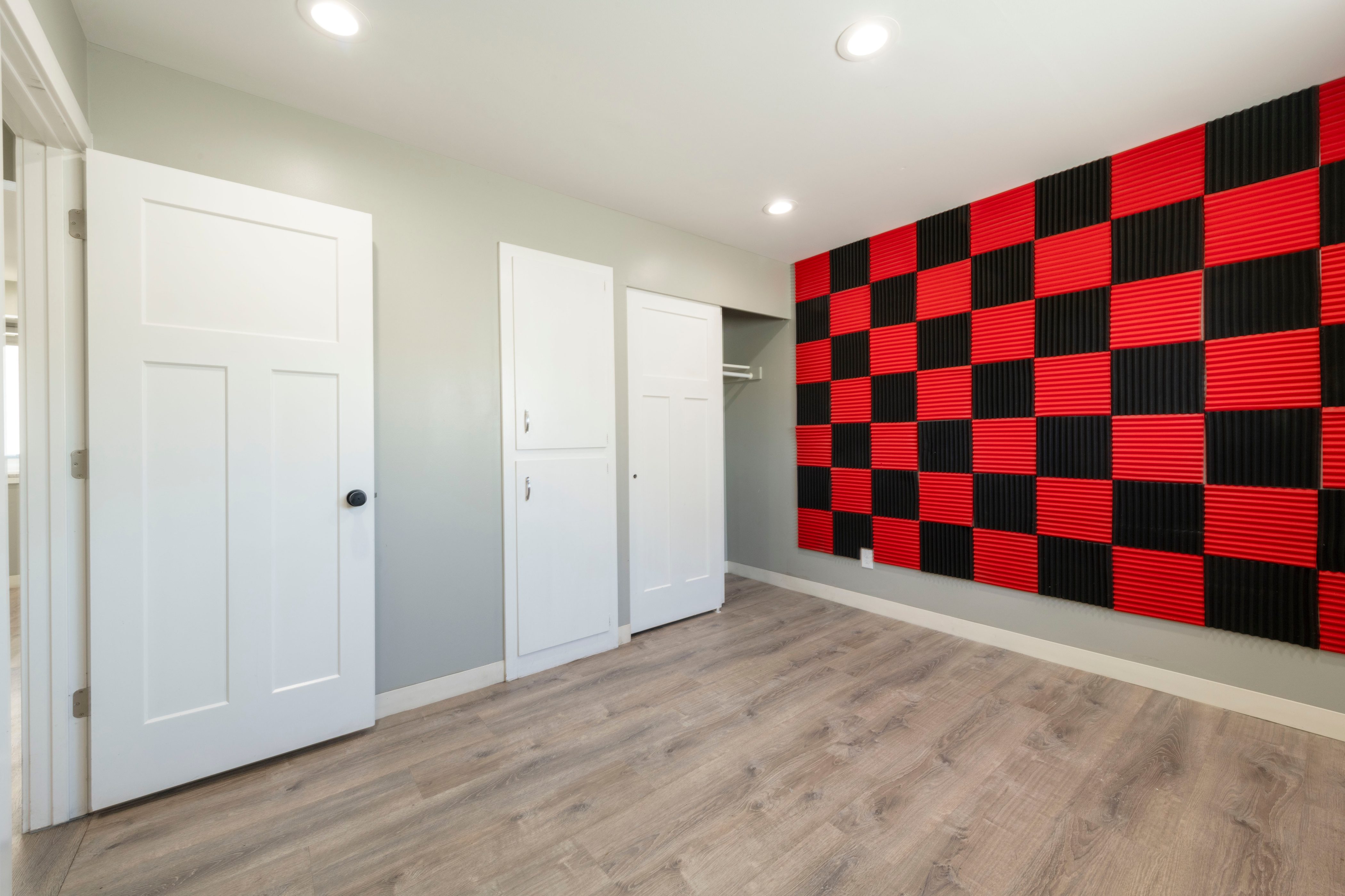 Open room featuring wood-finish flooring, recessed lighting, and a checkered red and black acoustic panel wall