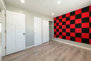 Open room featuring wood-finish flooring, recessed lighting, and a checkered red and black acoustic panel wall