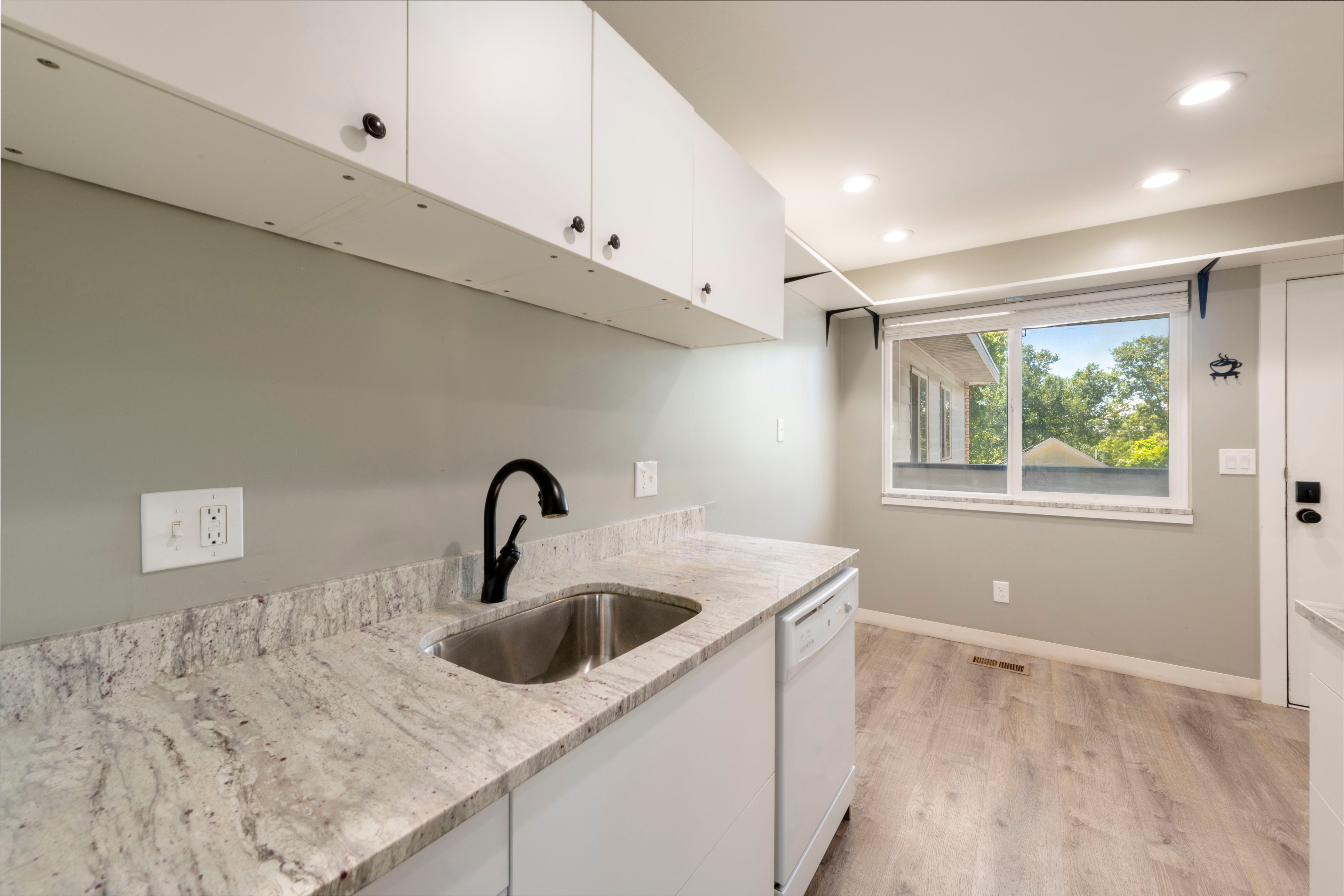 Utility area featuring white upper cabinetry, a stainless steel sink with a matte black faucet, light-toned patterned countertops, and wood-finish flooring