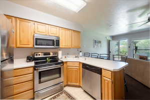 Kitchen featuring light wood cabinetry, stainless steel appliances, a white solid surface countertop, and a built-in dishwasher