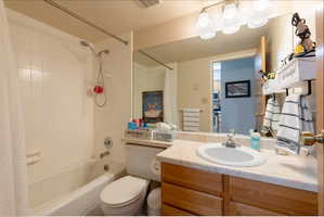 Full bathroom featuring a tub and shower combination with white tile surround, wood-finish vanity with a single basin sink, and a large wall-mounted mirror with overhead lighting