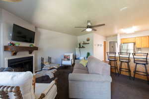 Living area featuring a fireplace with a wood mantle, ceiling fan, and carpeted flooring