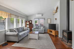 Living area featuring wood-finish flooring, a freestanding wood-burning stove with a stone hearth, and multiple windows providing natural light