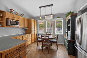 Kitchen area featuring abundant wood cabinetry, integrated microwave, stainless steel refrigerator, and a dining nook with a three-light pendant fixture