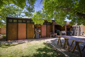 Backyard featuring a wooden utility structure with multiple entry points and transom windows, a gravel-covered area, and a section of manicured lawn