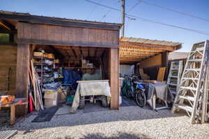 Wood-sided outdoor storage structure with an open bay, gravel flooring, and an additional covered outdoor area featuring a corrugated metal roof