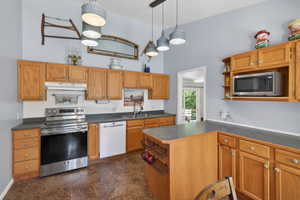 Kitchen featuring wood cabinetry, dark countertops, a stainless steel range, and a white dishwasher