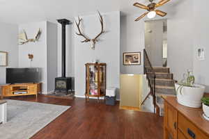 Living area featuring wood-finish flooring, a black cast iron wood-burning stove with a stovepipe, and a carpeted staircase with a dark metal railing