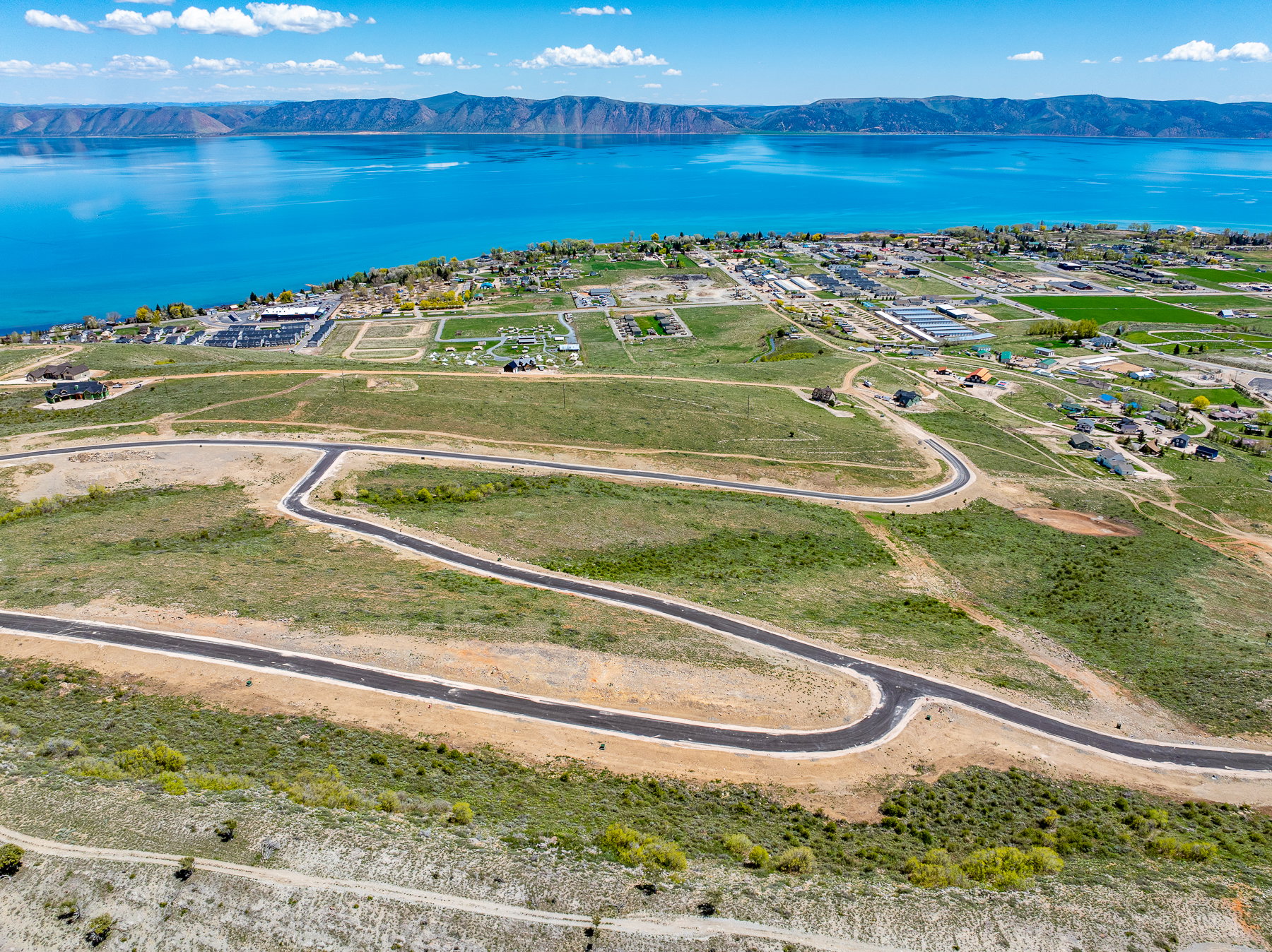 Expansive land parcel featuring paved roads, scattered green vegetation, and distant body of water