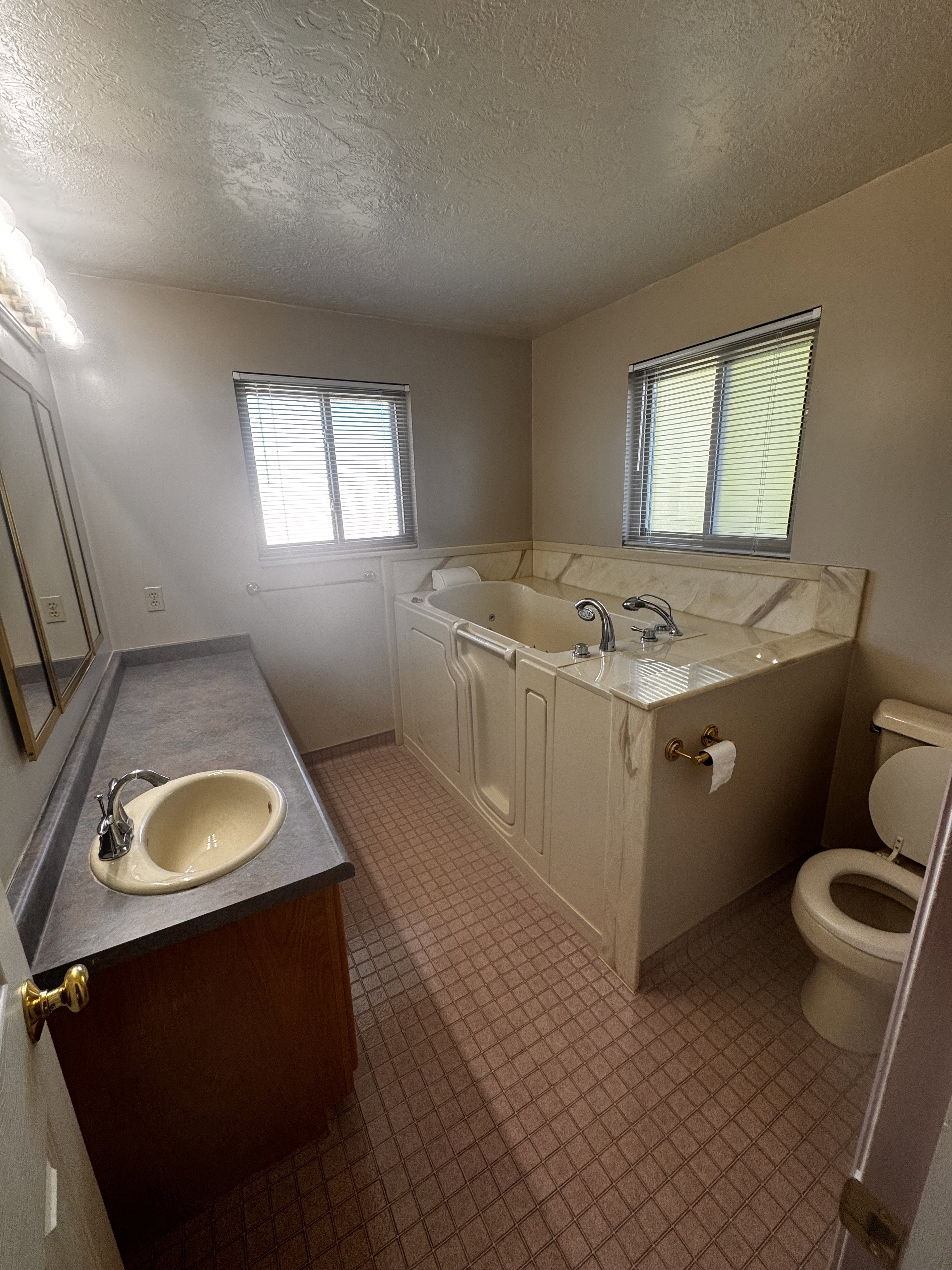 Bathroom featuring a built-in jetted tub, a single vanity with a laminate countertop, and a toilet