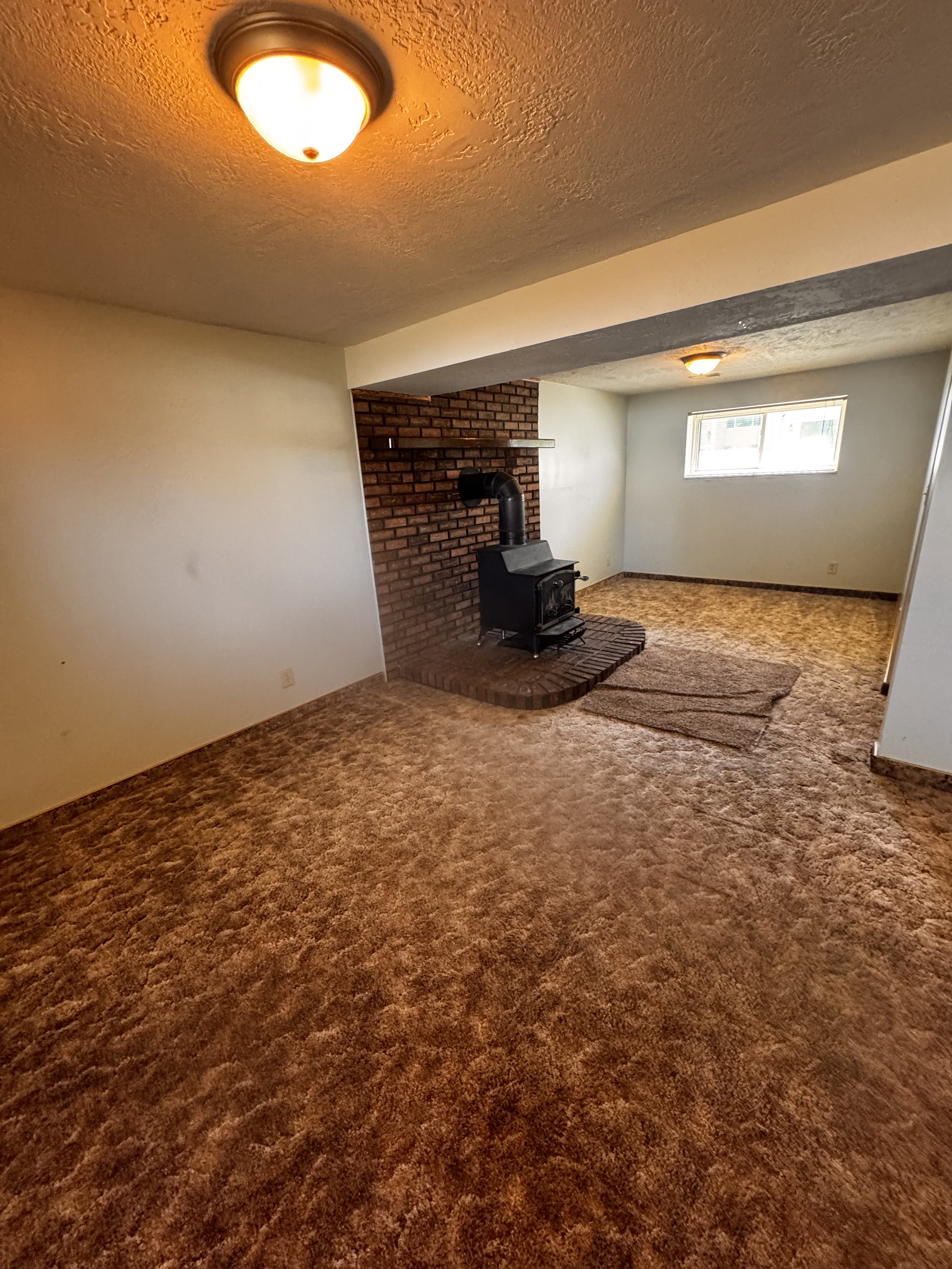 Interior space featuring a brick fireplace with a black wood-burning stove, textured ceiling, flush-mount lighting, and a window with white trim