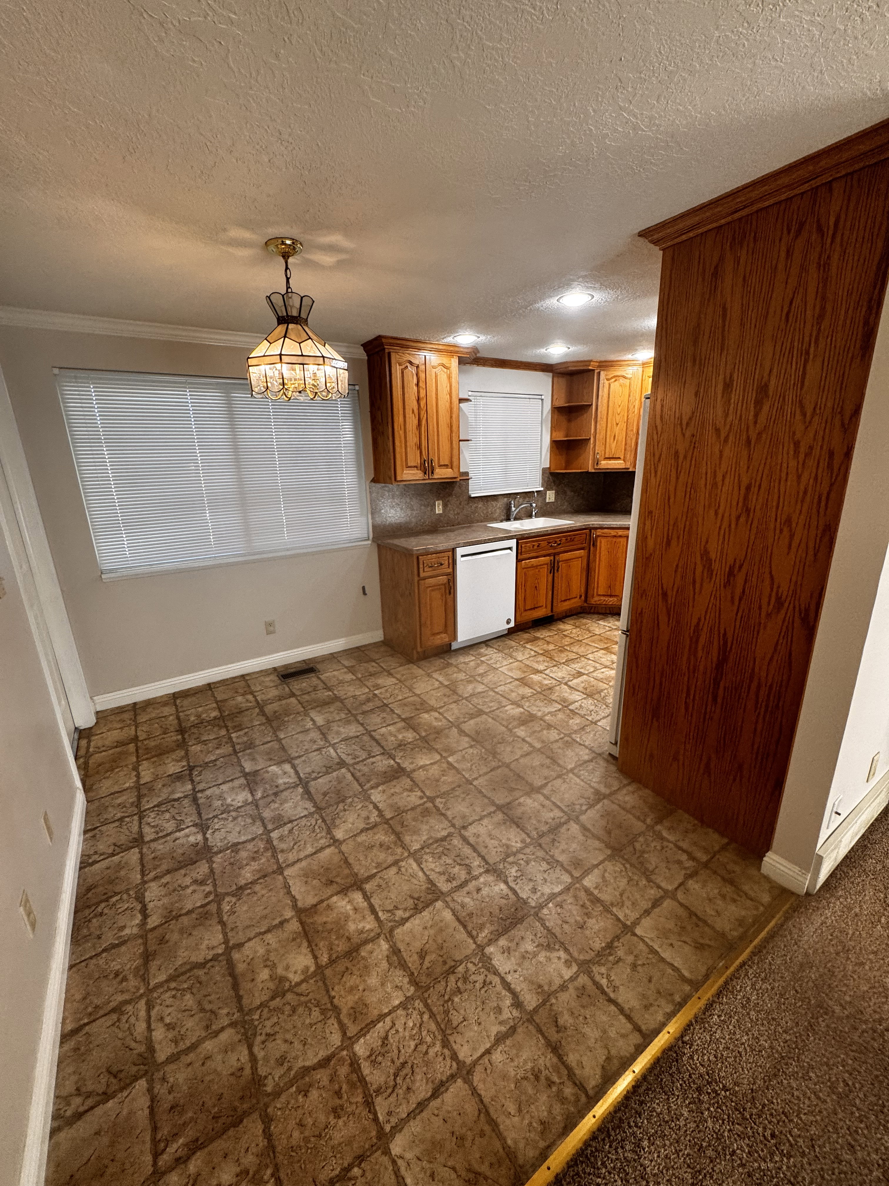 Kitchen area featuring a tiled floor, wood cabinetry, built-in dishwasher, recessed lighting, and a decorative pendant light fixture