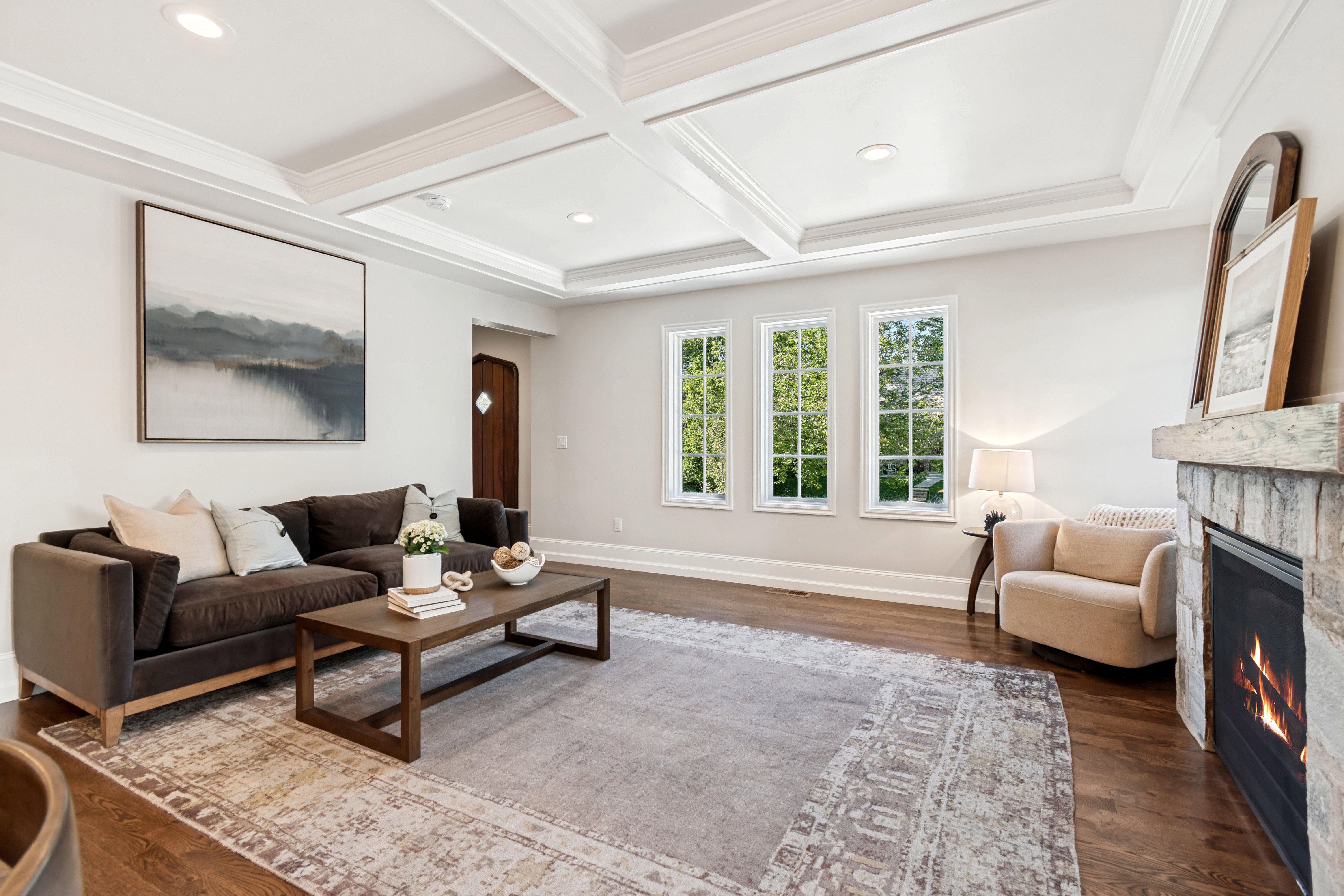 Living area featuring wood-finish flooring, a coffered ceiling, stone-clad fireplace, and multiple windows