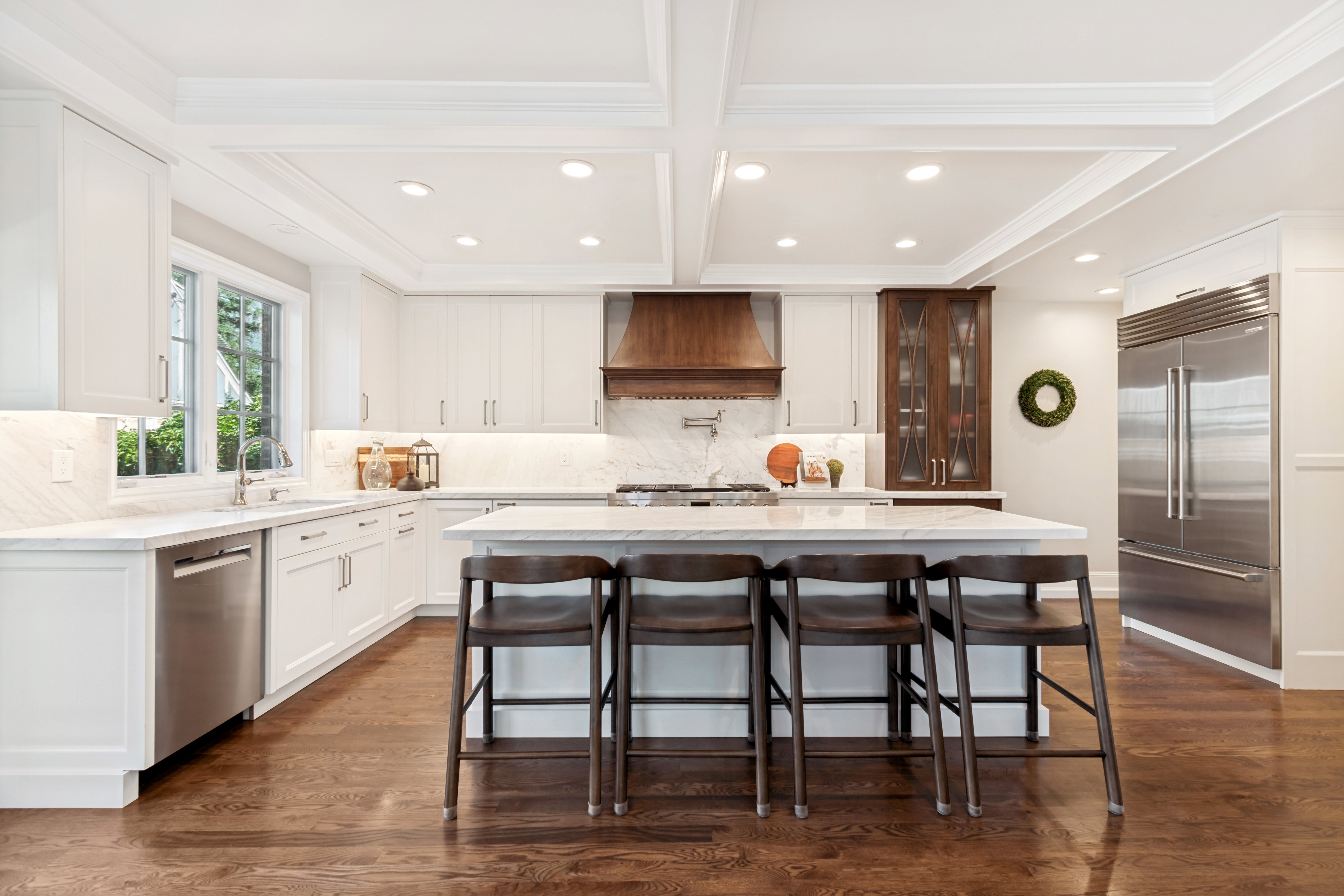 Gourmet kitchen featuring a large central island, coffered ceiling, stainless steel appliances, wood-finish flooring, and ample white cabinetry