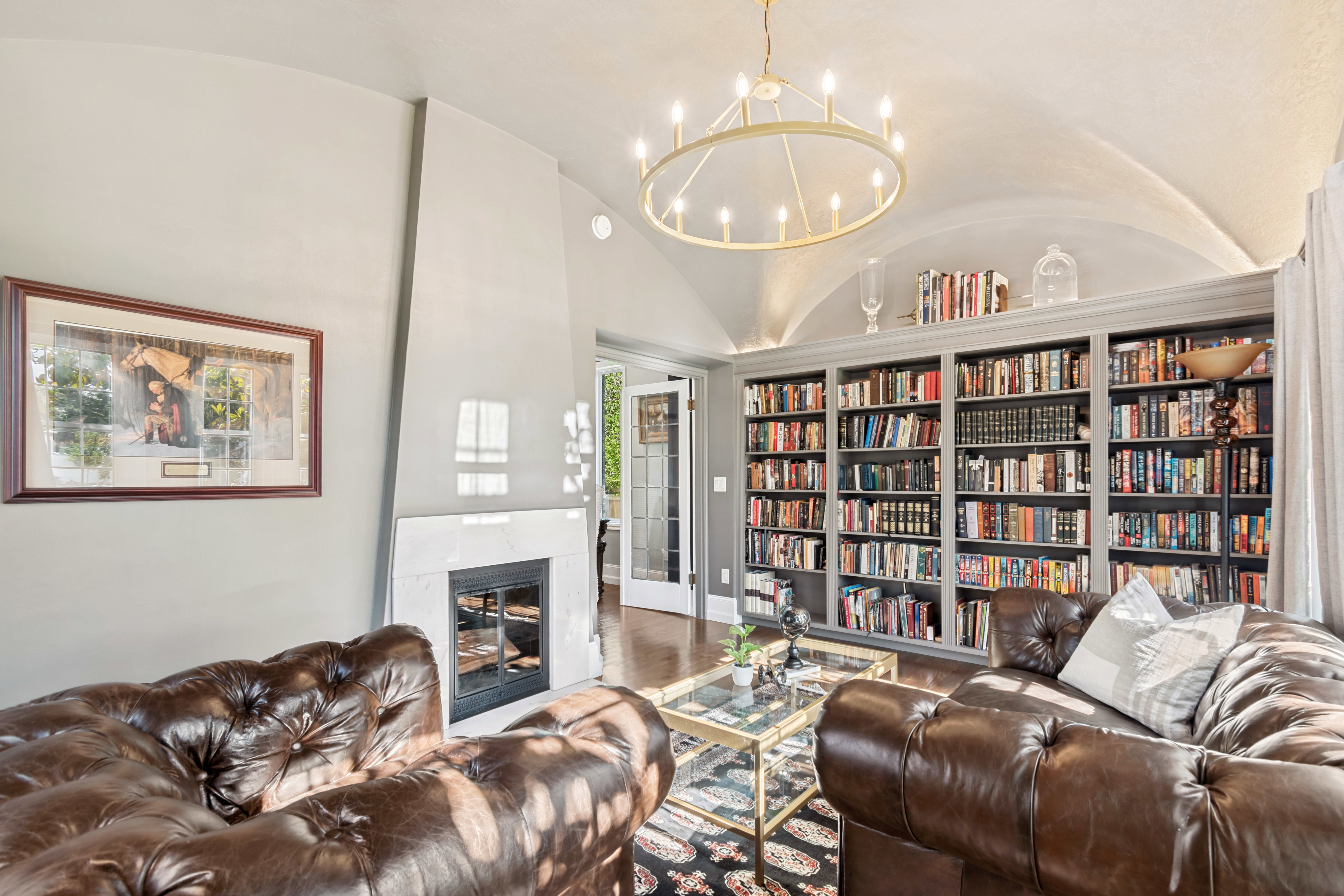 Vaulted ceiling room featuring extensive built-in bookcases, a fireplace with a light-toned surround, hardwood flooring, and a circular chandelier