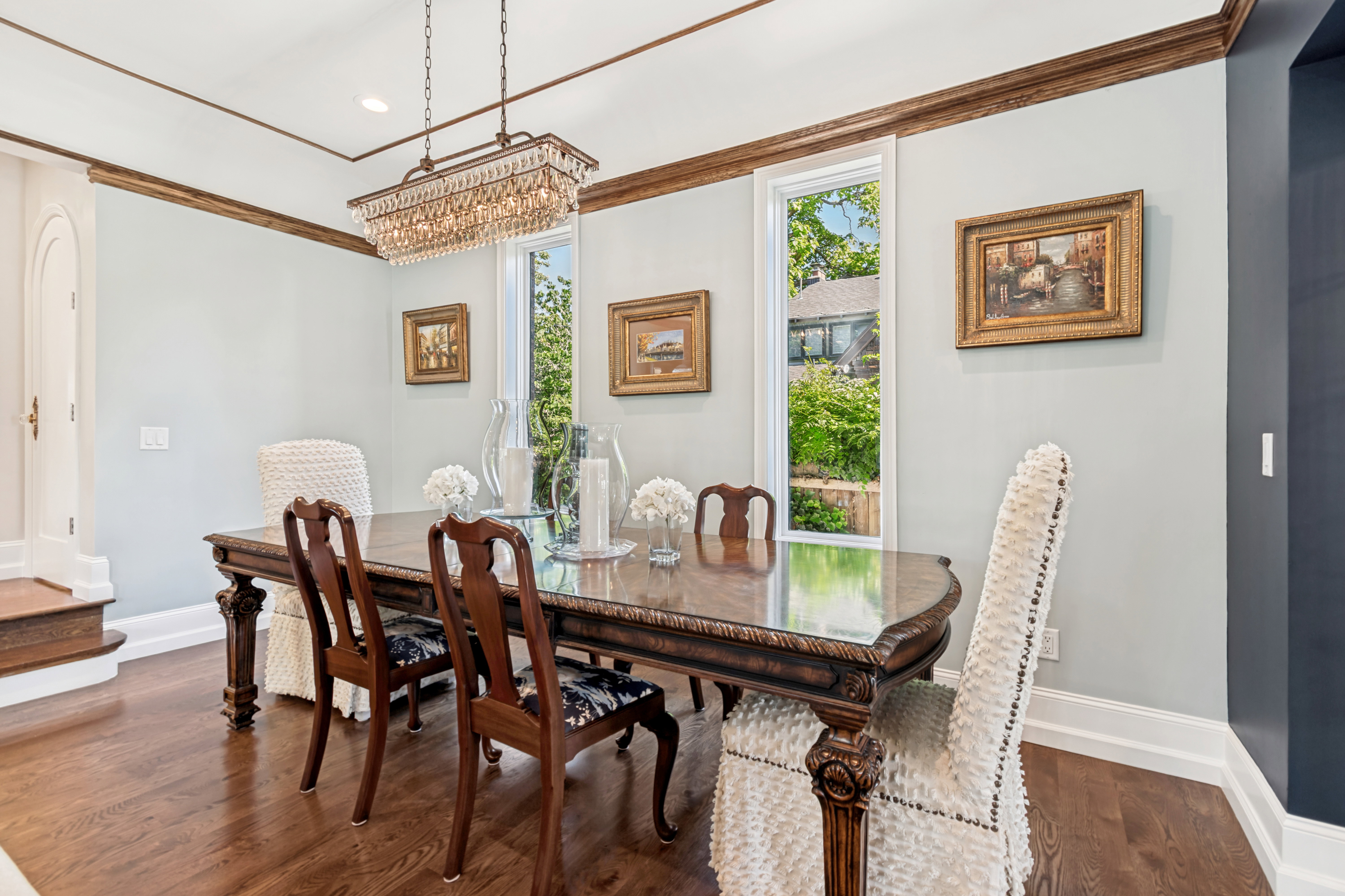 Formal dining area featuring rich wood-finish flooring, a tray ceiling with crown molding, and a crystal chandelier